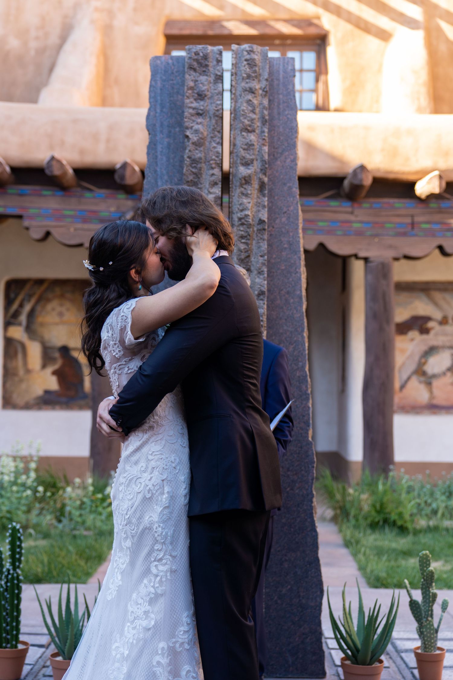 A romantic couple shares a tender embrace in a Spanish-style courtyard with columns and greenery.