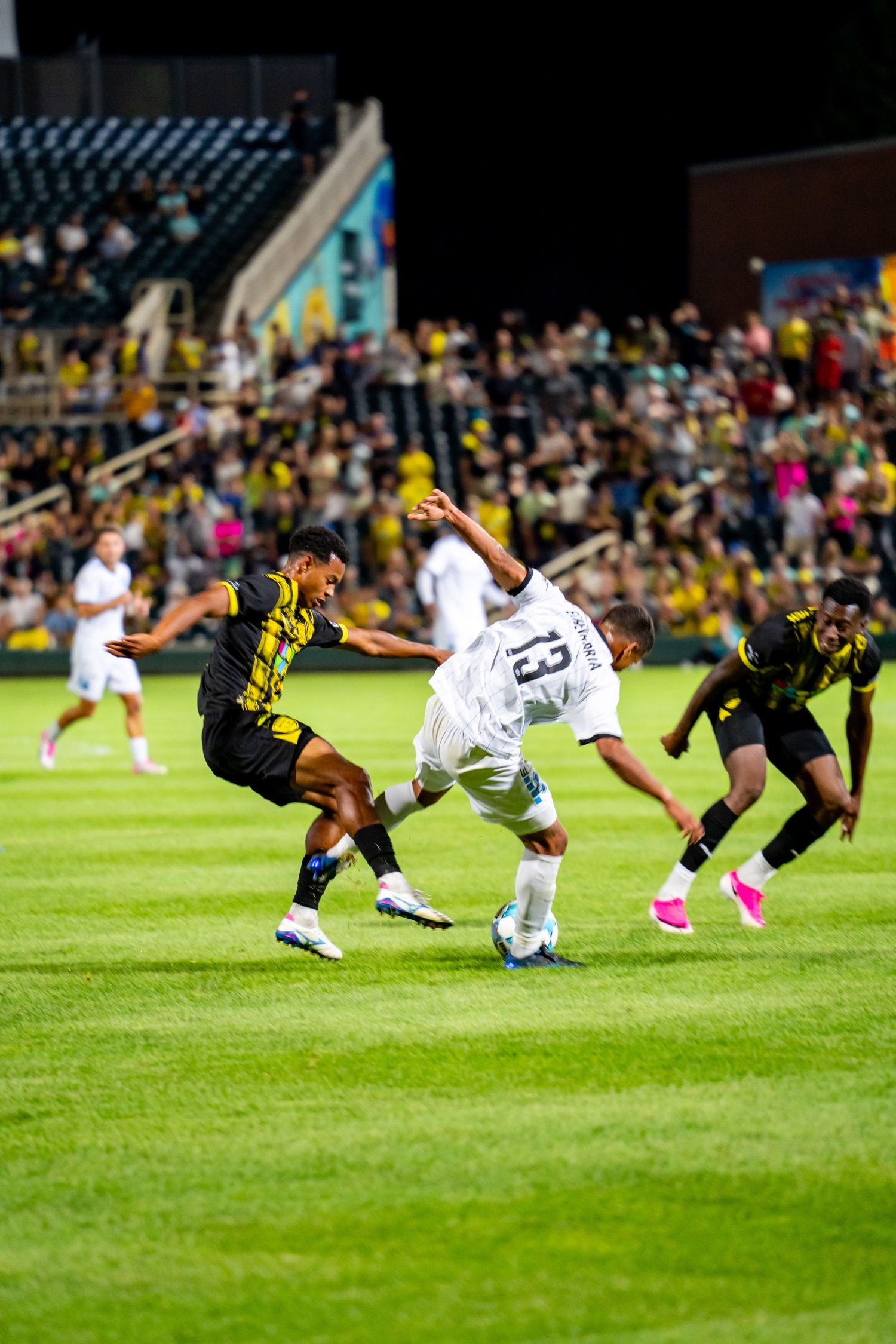 Soccer players in black and white uniforms compete for the ball on a green field during a night match.