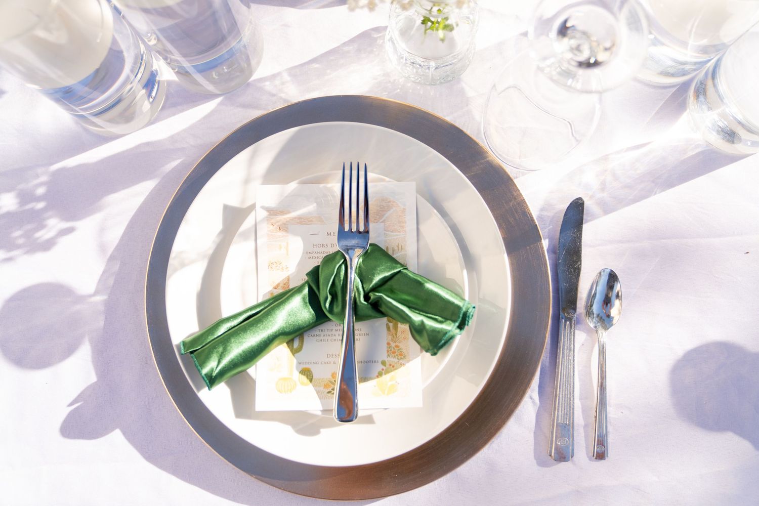 Elegant place settings with wine glasses and silverware arranged on white plates at a formal event.