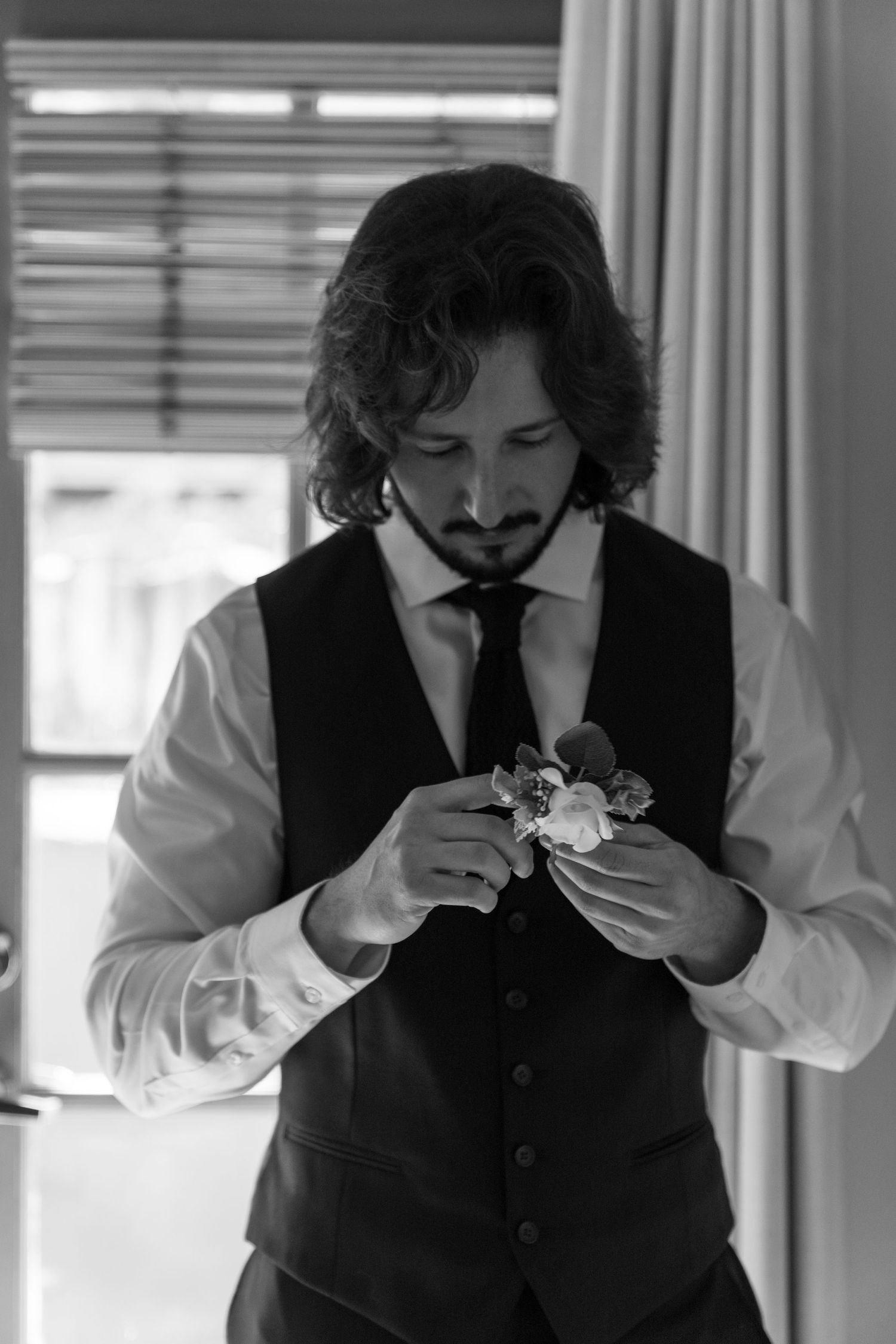 A person in formal attire carefully pins a boutonniere flower to their vest.