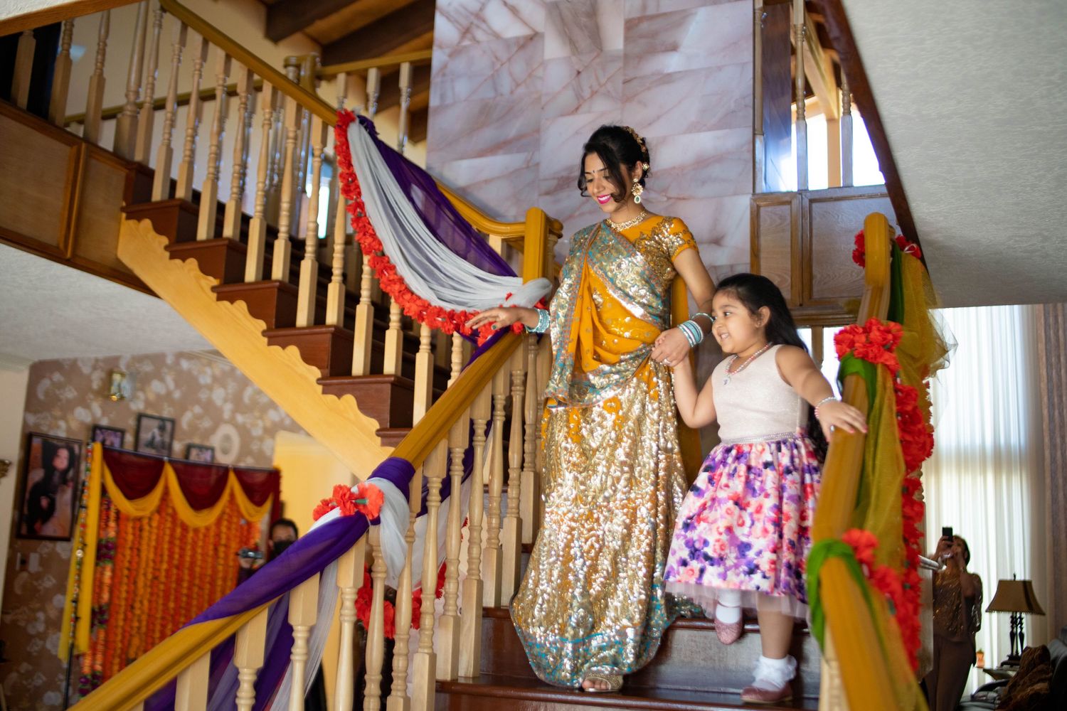 People in colorful traditional clothing dance together during a festive celebration in an indoor setting.