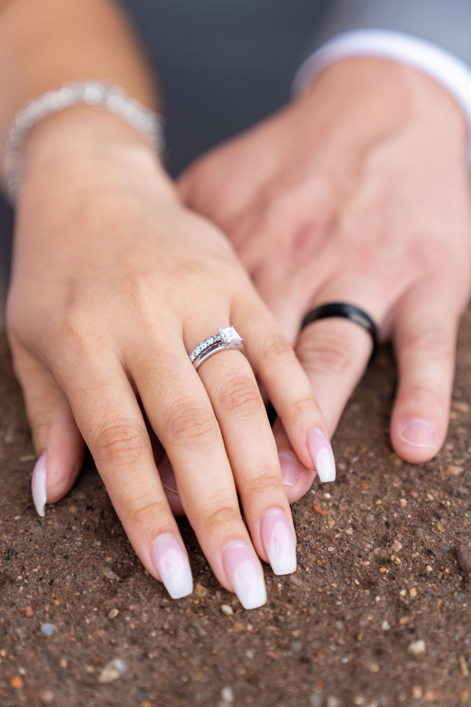 Close-up of hands with wedding rings touching soil in a symbolic planting gesture.