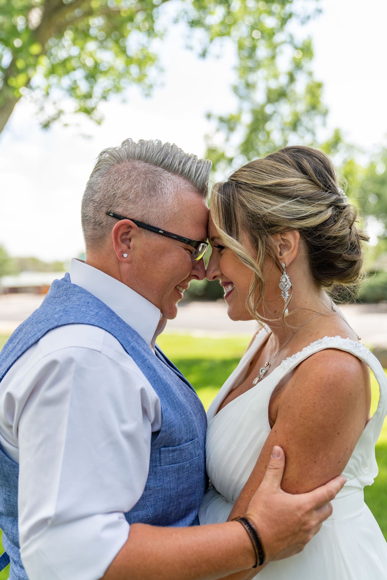 A loving couple shares an intimate moment in their wedding attire against a sunny outdoor backdrop.