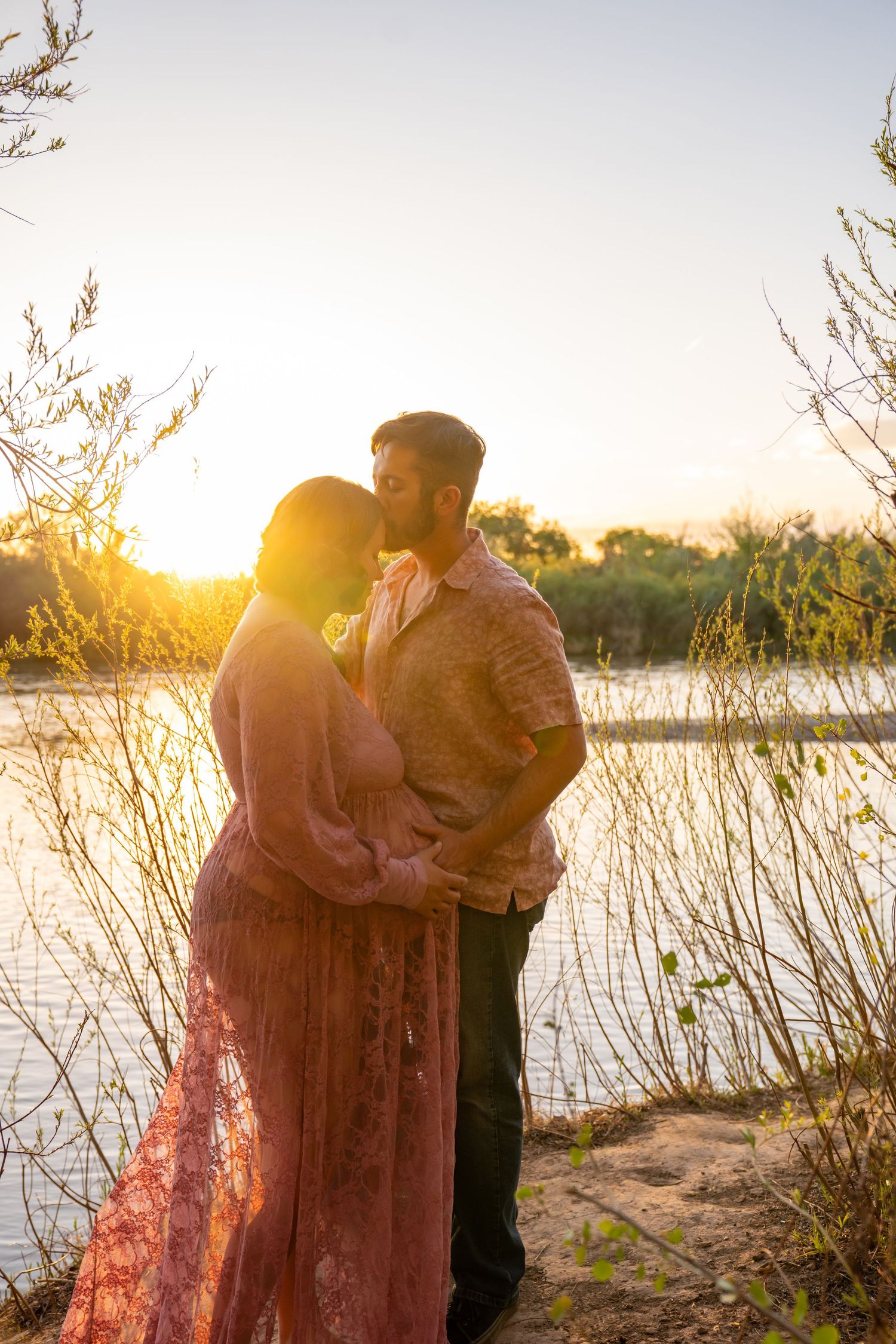 A romantic sunset silhouette by a lake with warm golden light filtering through trees.
