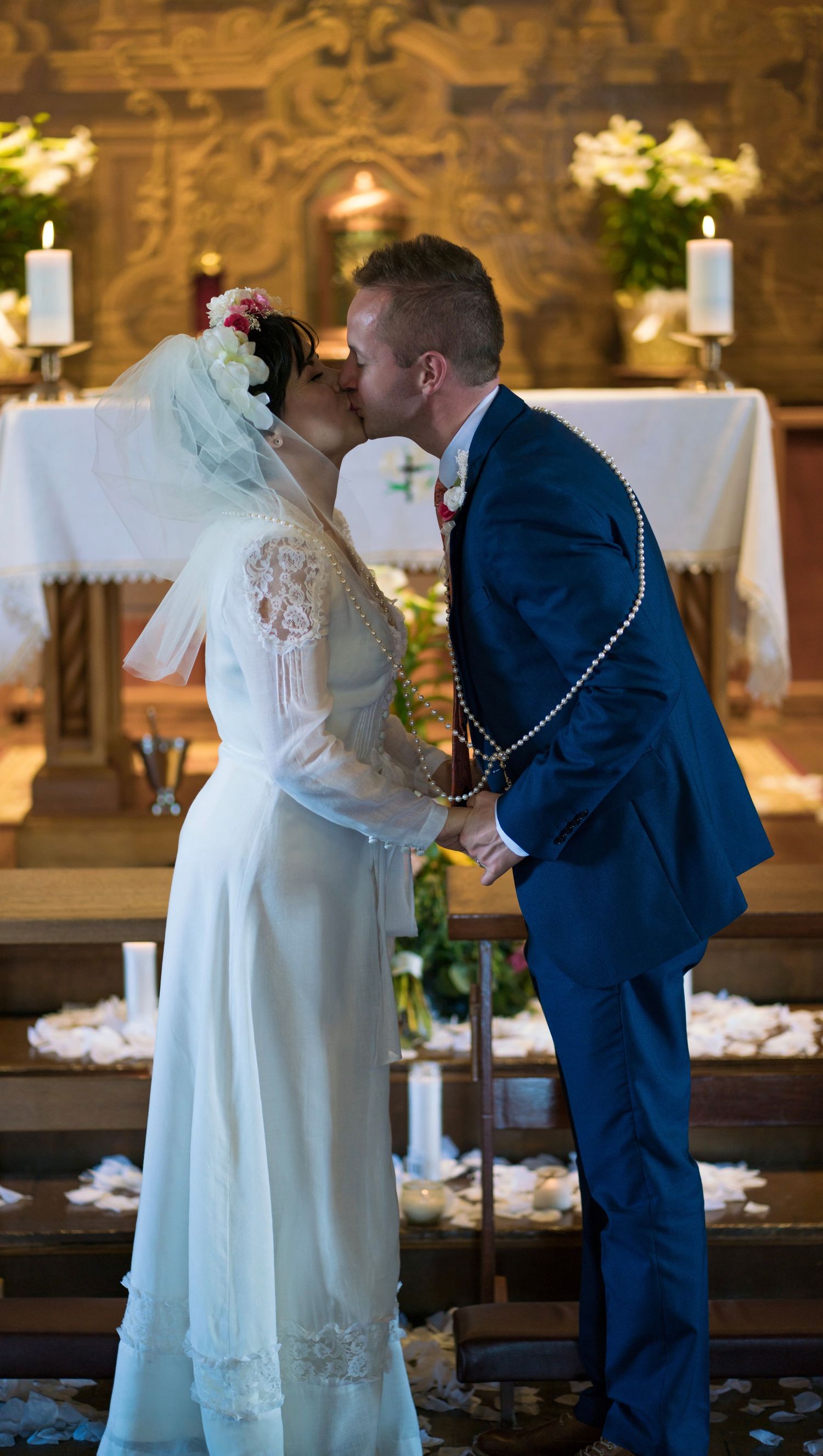 A romantic wedding couple shares a tender kiss in a beautifully lit church setting with glowing candles in the background.
