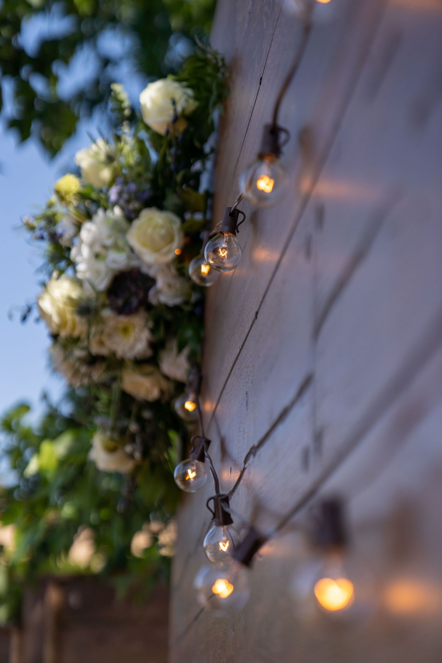 String lights and white floral arrangements create an elegant outdoor ambiance at dusk.