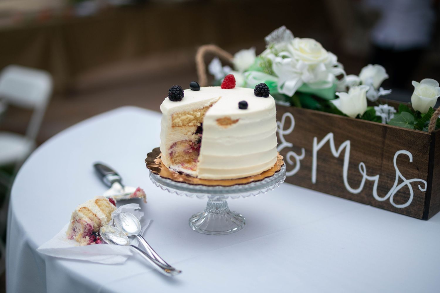 White frosted wedding cake with delicate floral decorations displayed on an elegant dessert table at a reception.
