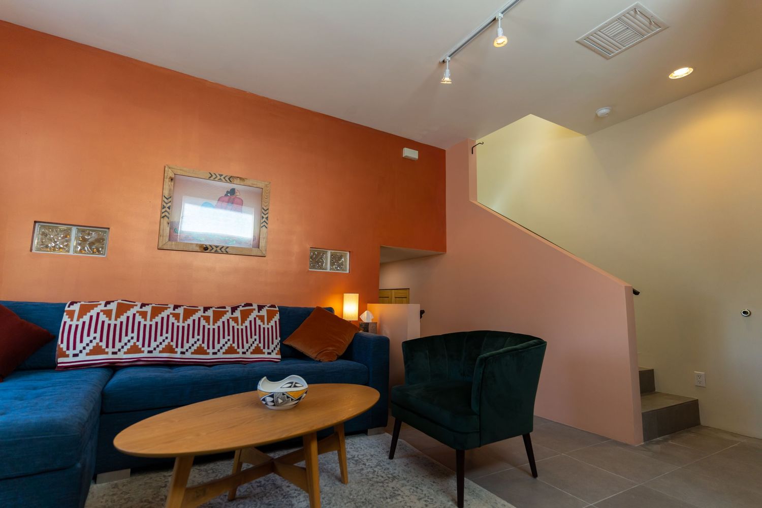 Modern office lounge area with orange accent walls, track lighting, and comfortable seating arrangements.
