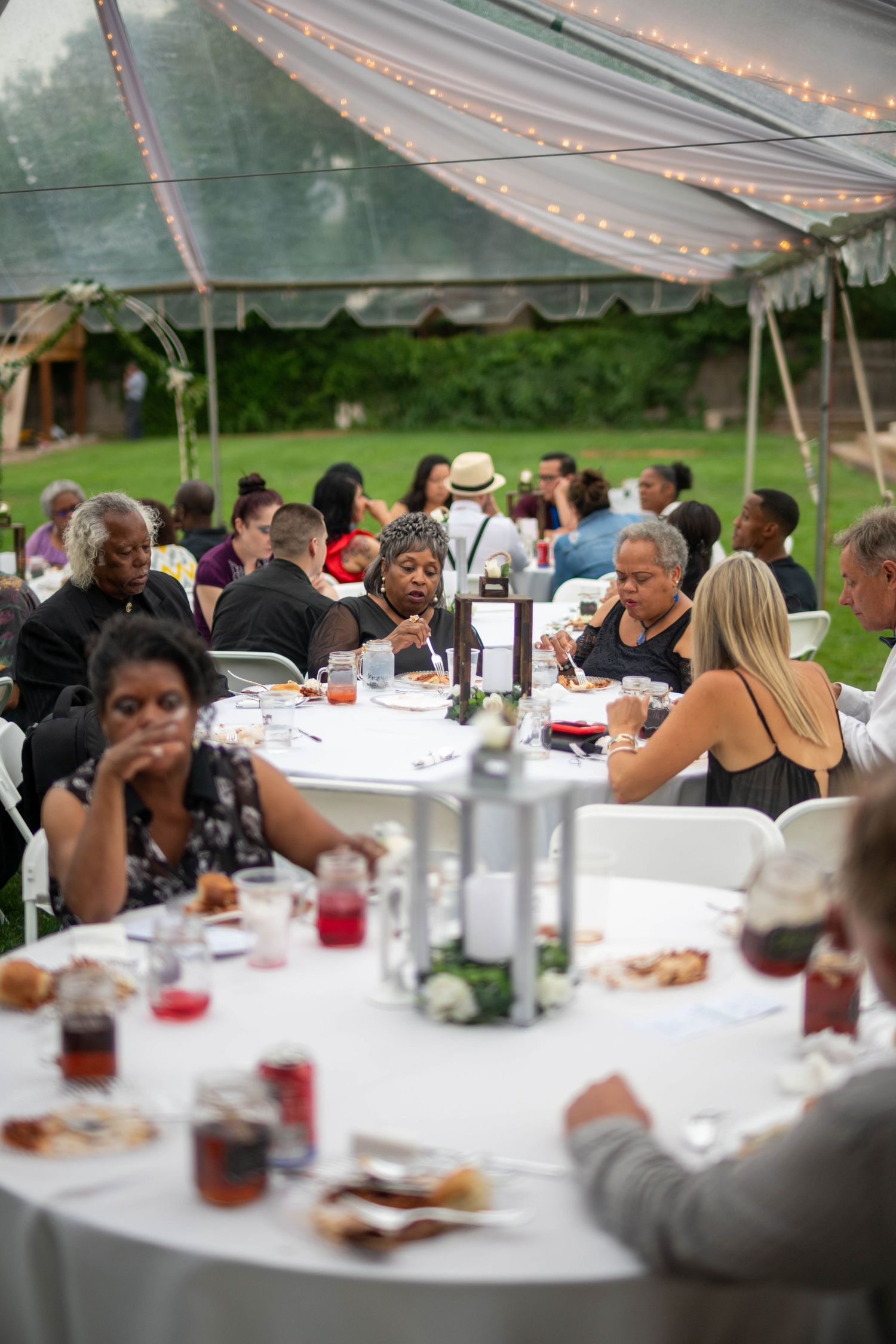 Guests dining under an elegant outdoor tent with string lights at a catered event celebration.