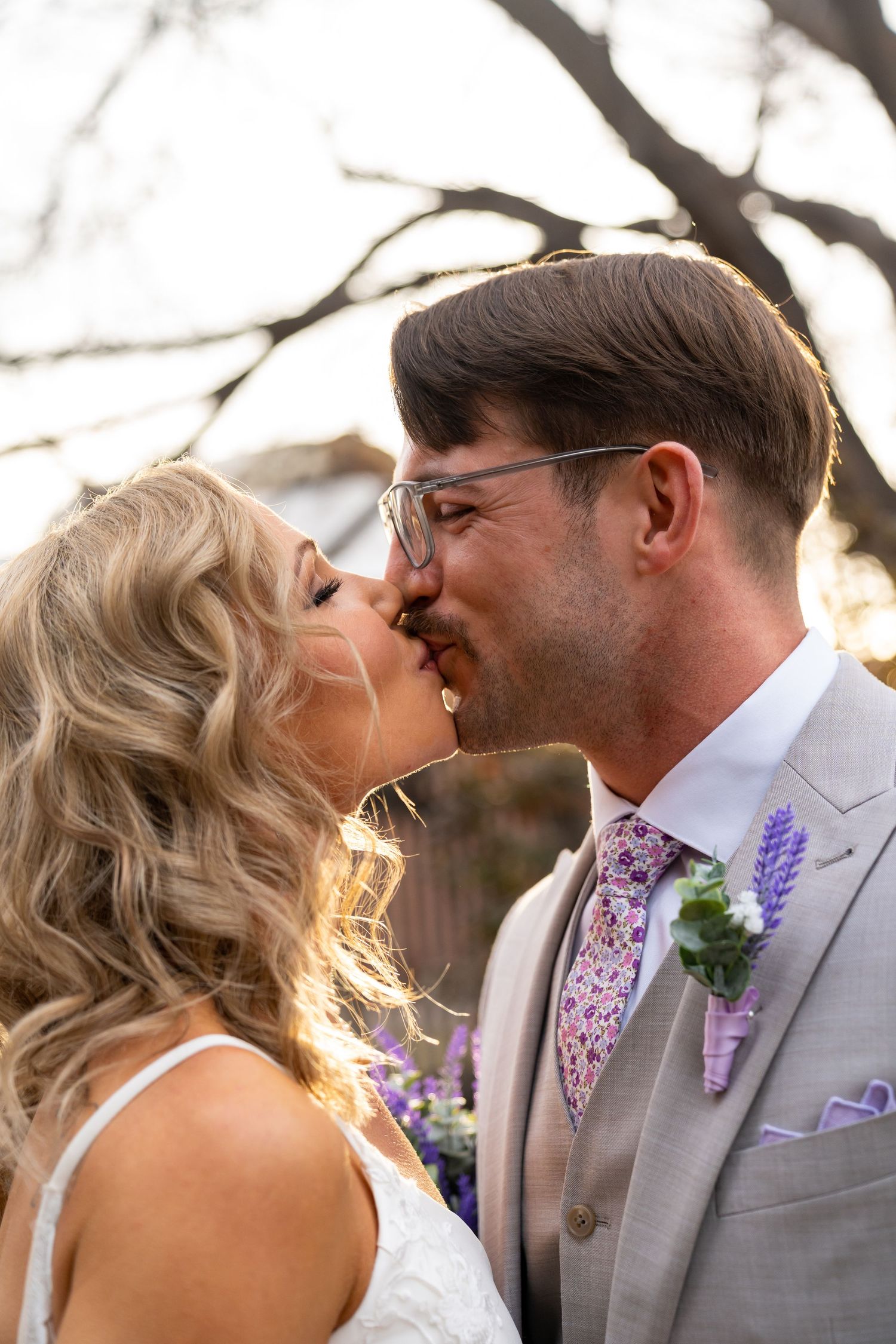 Wedding couple shares romantic kiss under blooming spring trees.