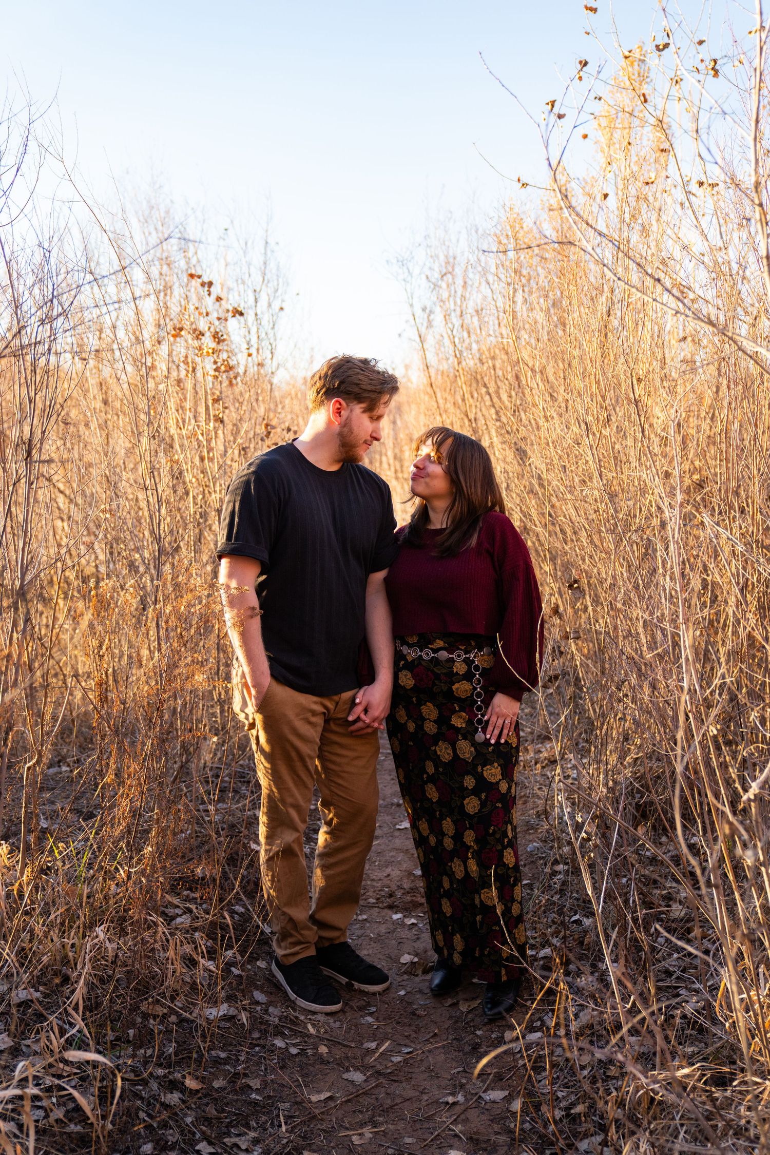Couple gazing at each other on a nature trail surrounded by golden dry grasses during golden hour.