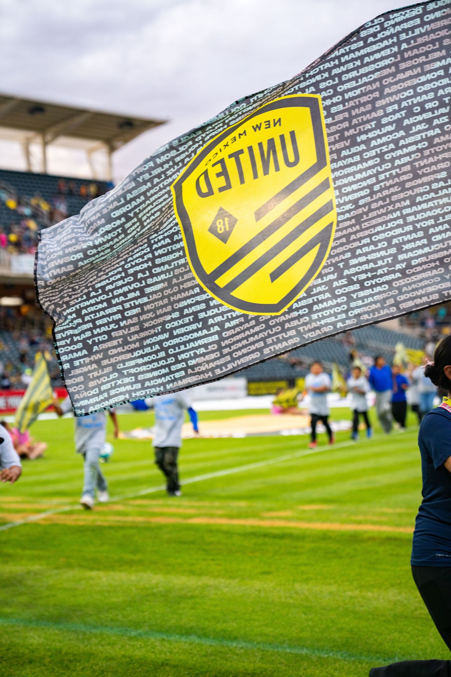New Mexico United soccer team flag waving on the field during a match at a stadium.