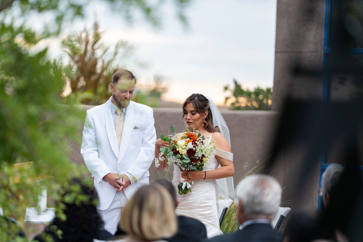 Outdoor wedding ceremony with white-clad officiant and floral arrangements.