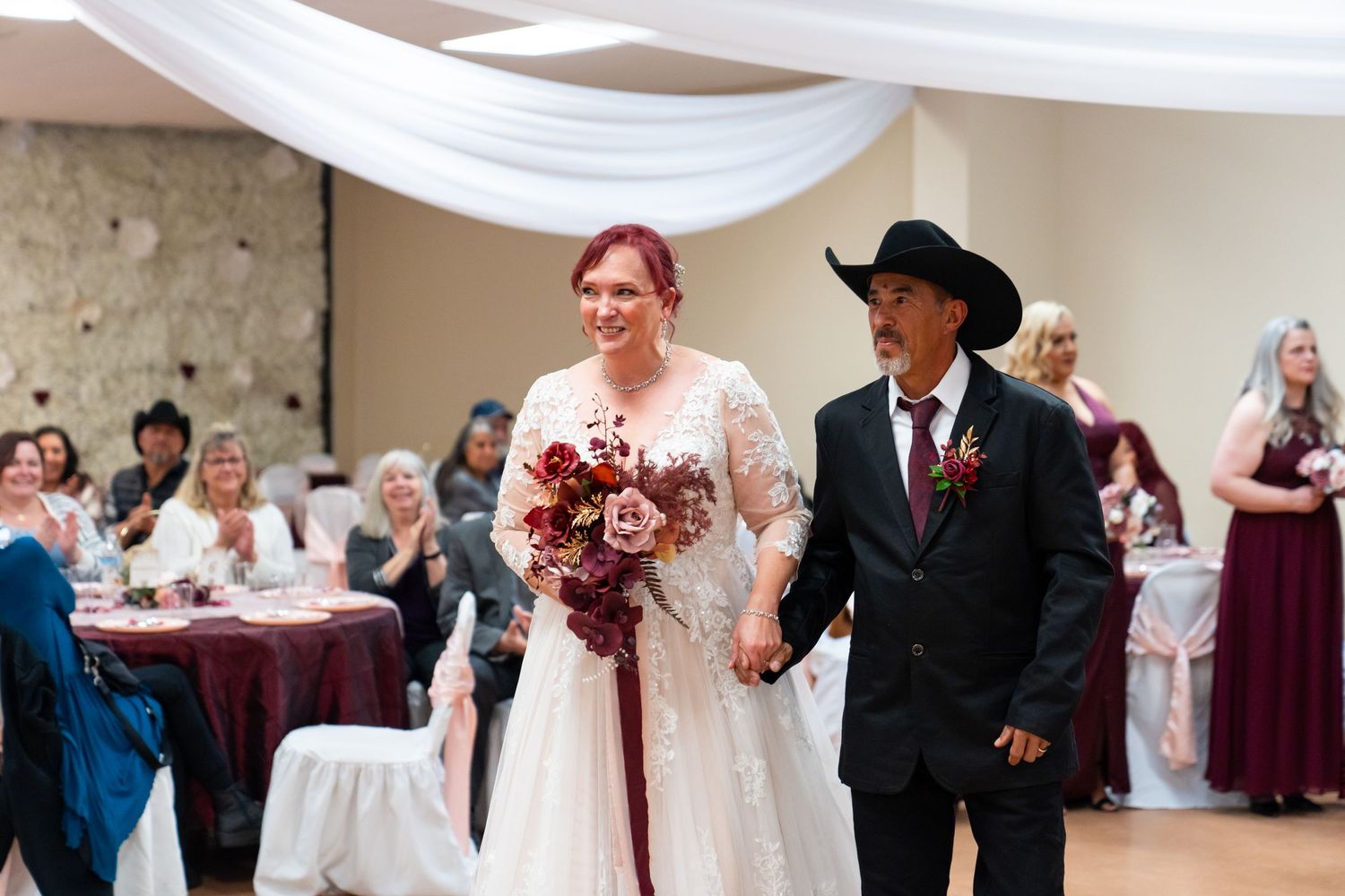 Wedding couple walking together in a reception hall decorated in burgundy and white.