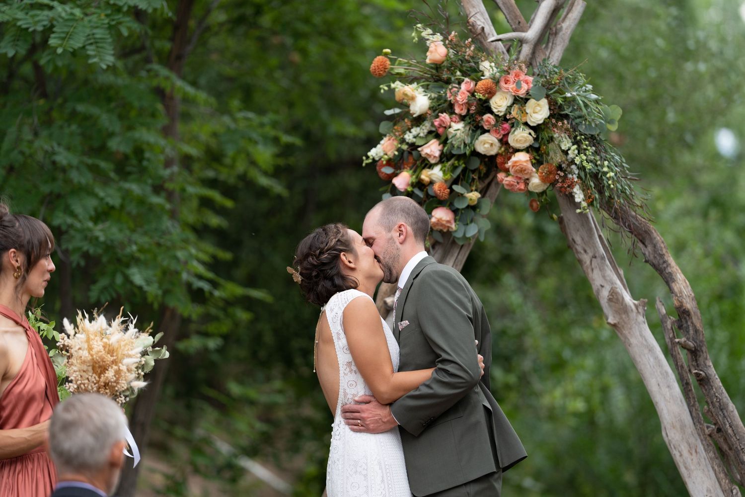Wedding couple embraces among blooming trees and pink flowers in garden setting.