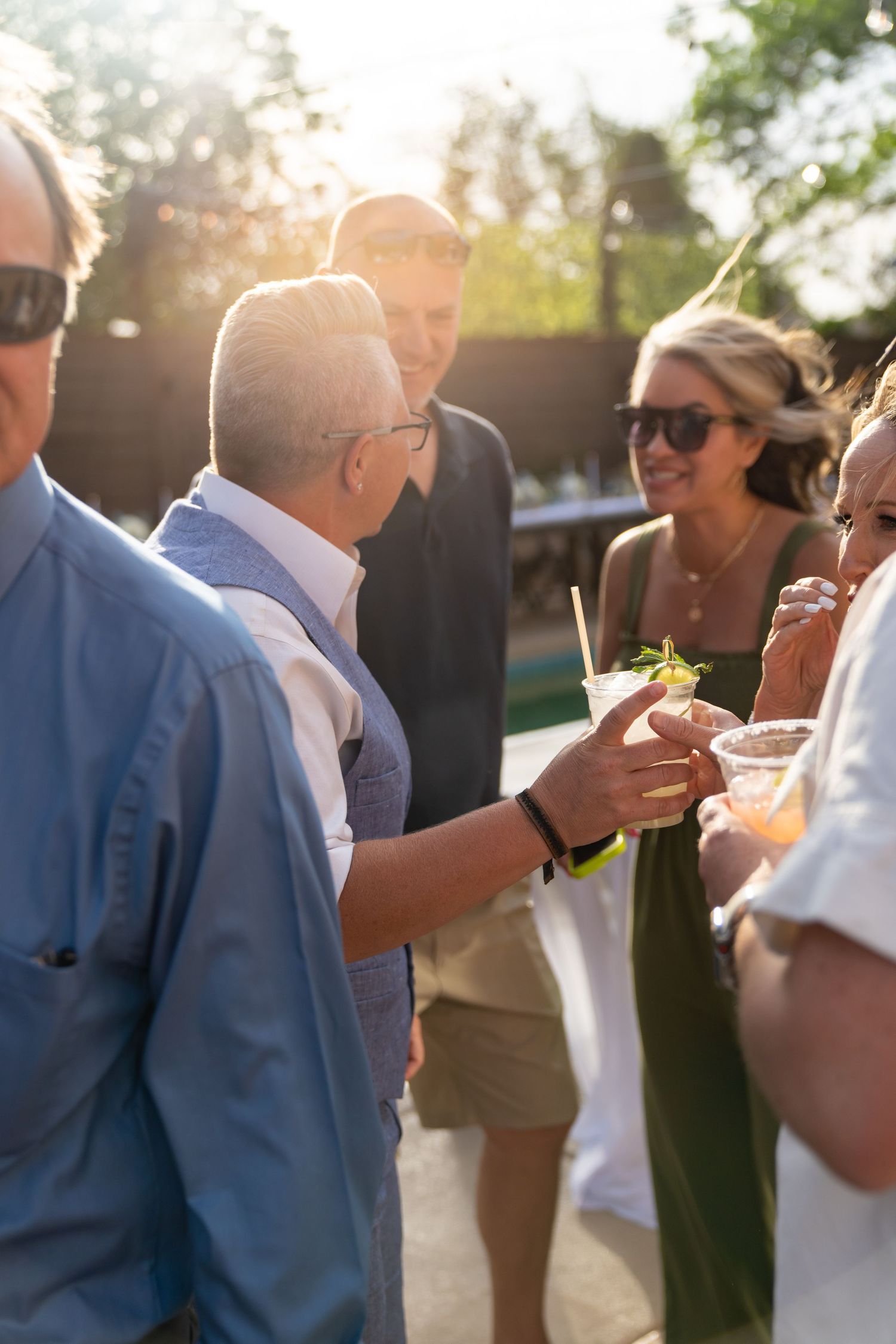 Wedding guests mingle and enjoy drinks during golden hour at outdoor reception.