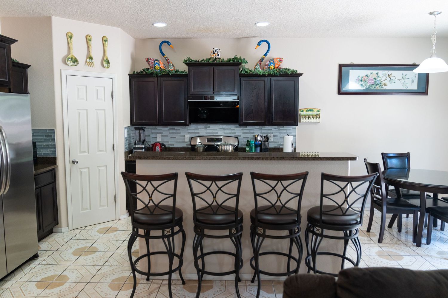 Modern kitchen and dining area with black appliances, bar seating, and decorative wall art featuring spoons.