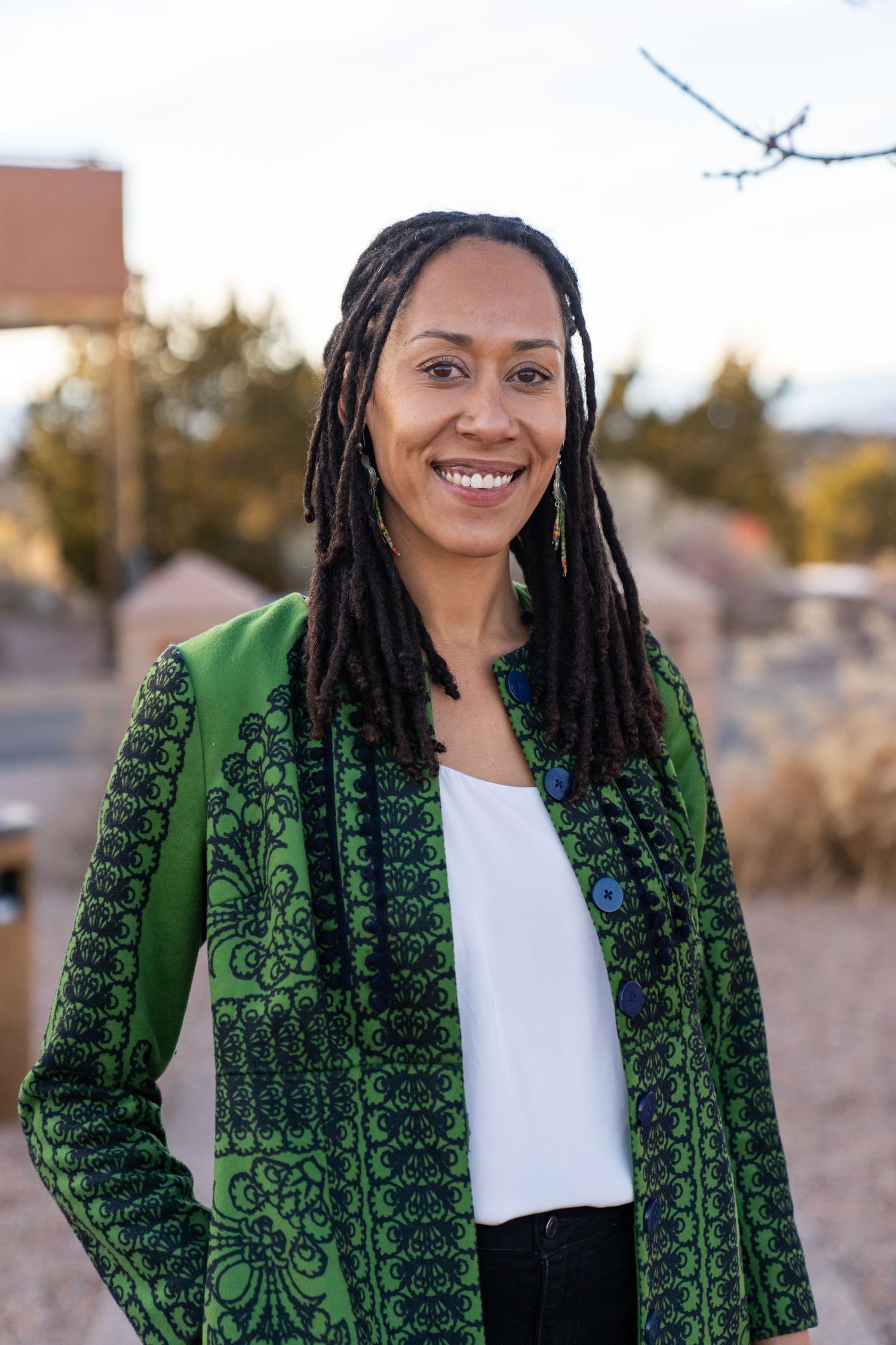 Person wearing elegant green embroidered jacket with white top in outdoor setting.