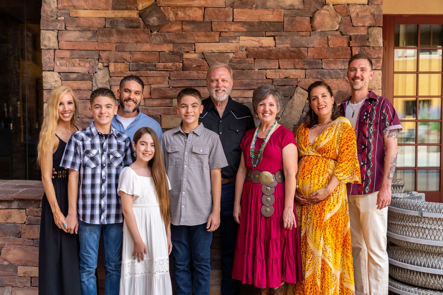 Family portrait of nine people standing together in front of a brick wall.