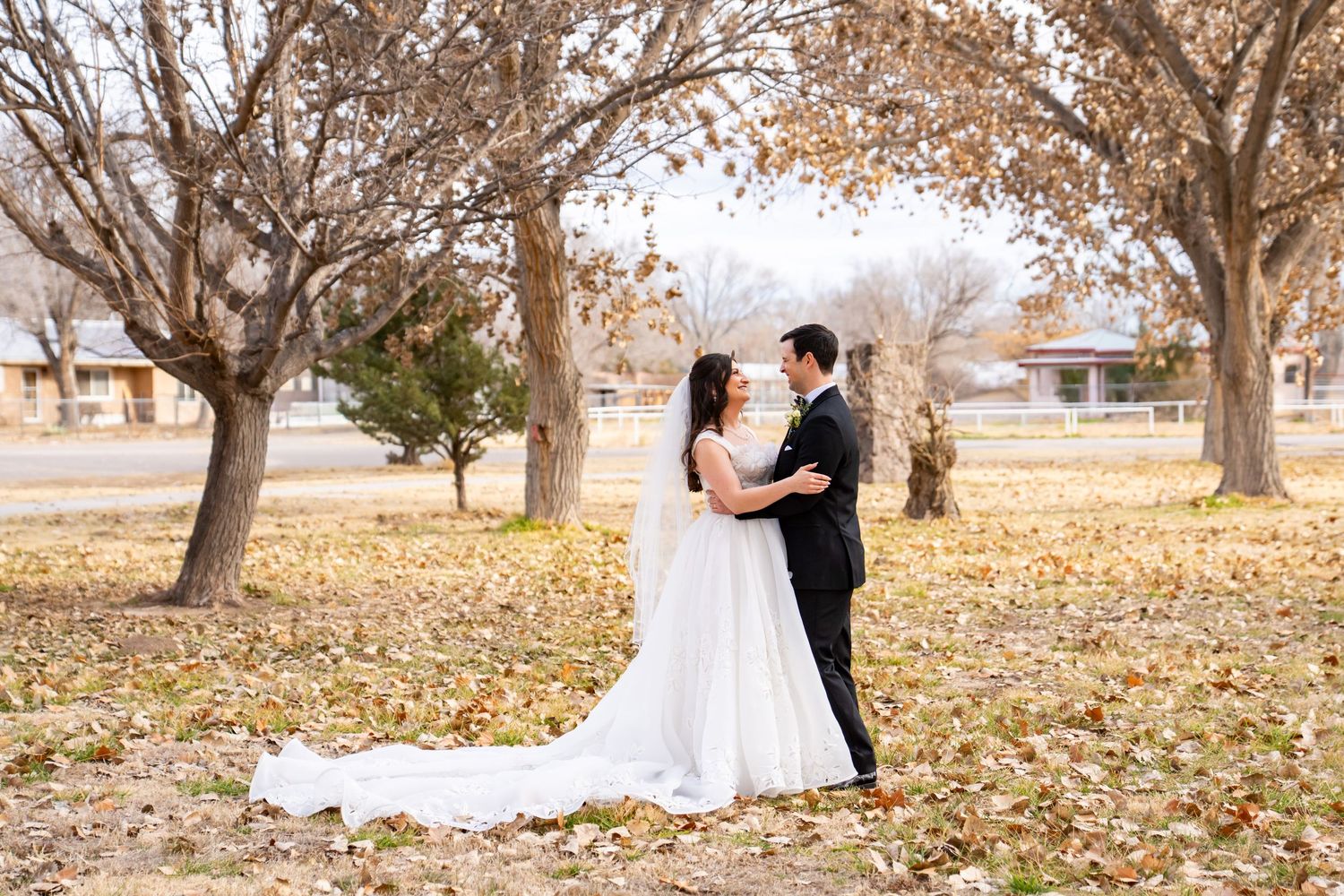 Bride and groom share a romantic moment among autumn trees covered in fallen leaves at an outdoor wedding.