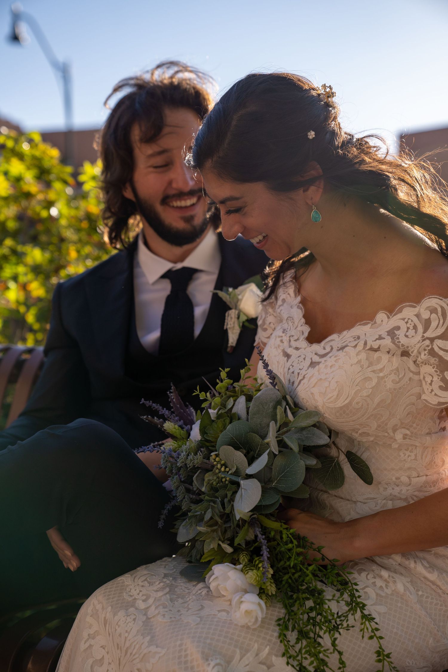 Wedding couple shares intimate moment with greenery and sunlight in background.