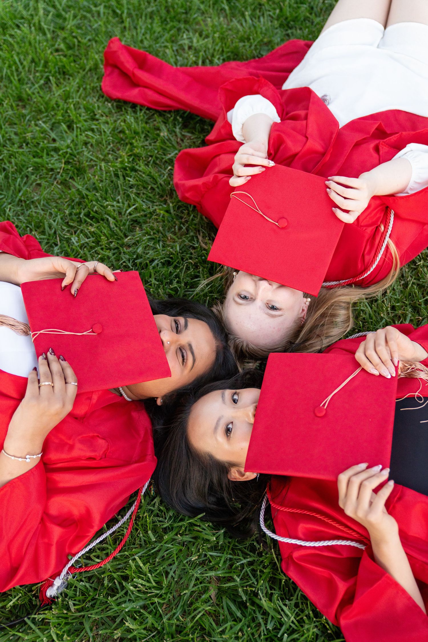 Graduates lying on grass holding red graduation caps.