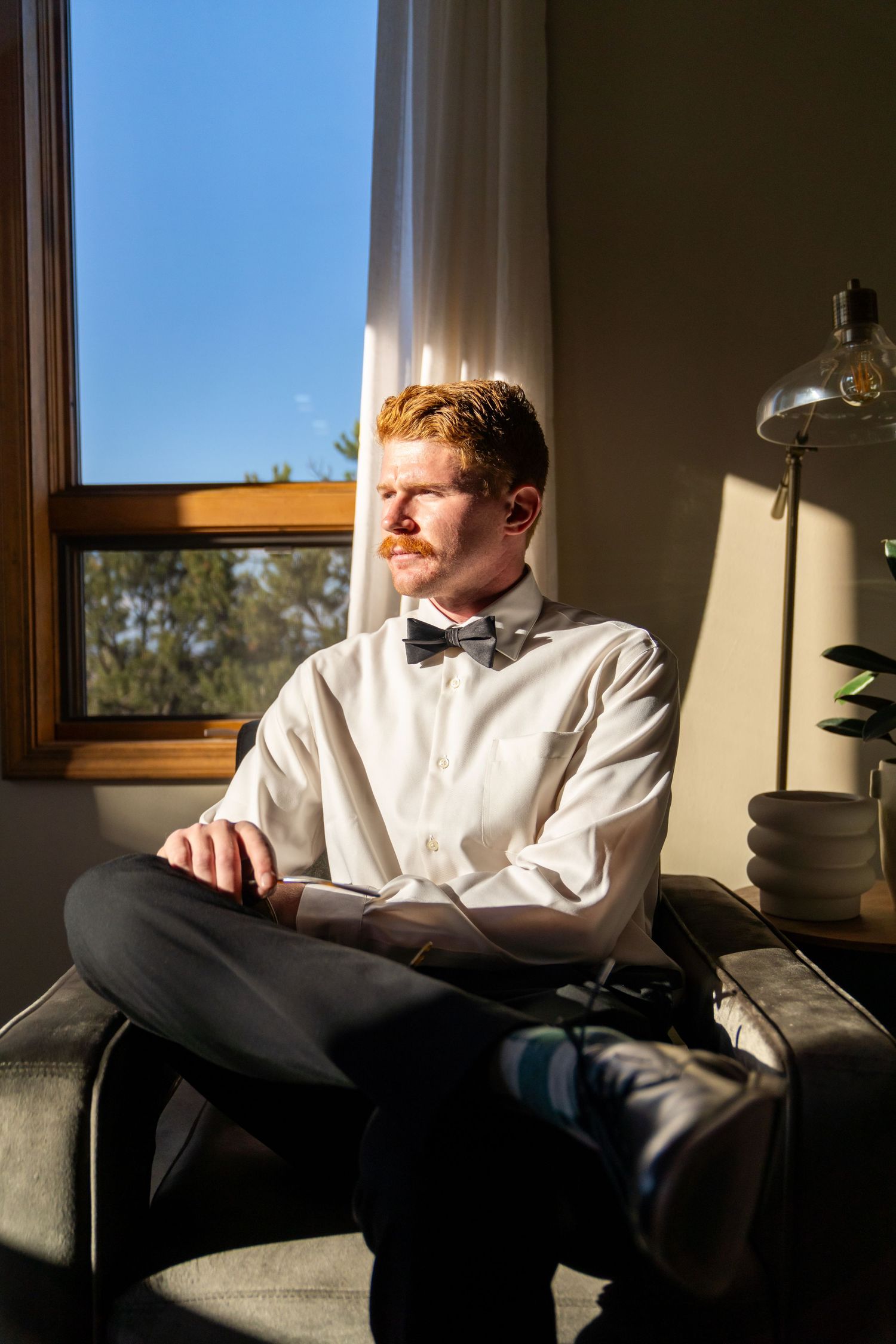 Person in white shirt relaxing on grey couch near window with natural lighting.