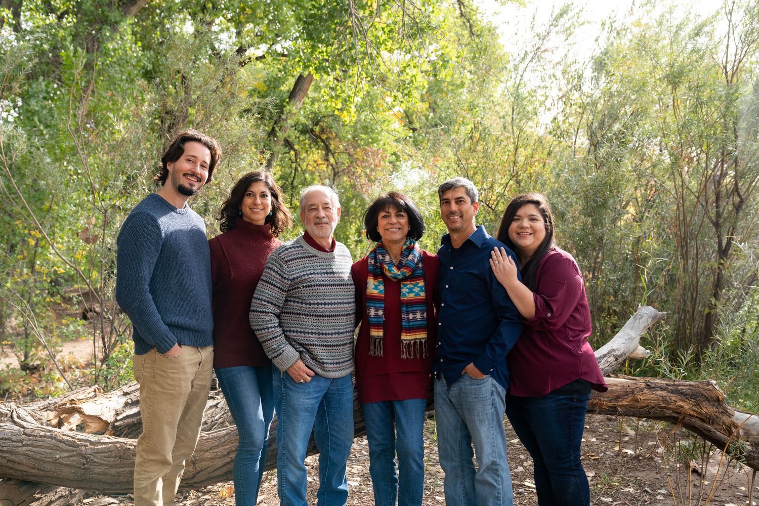Group photo of six people standing together outdoors in casual attire among trees.