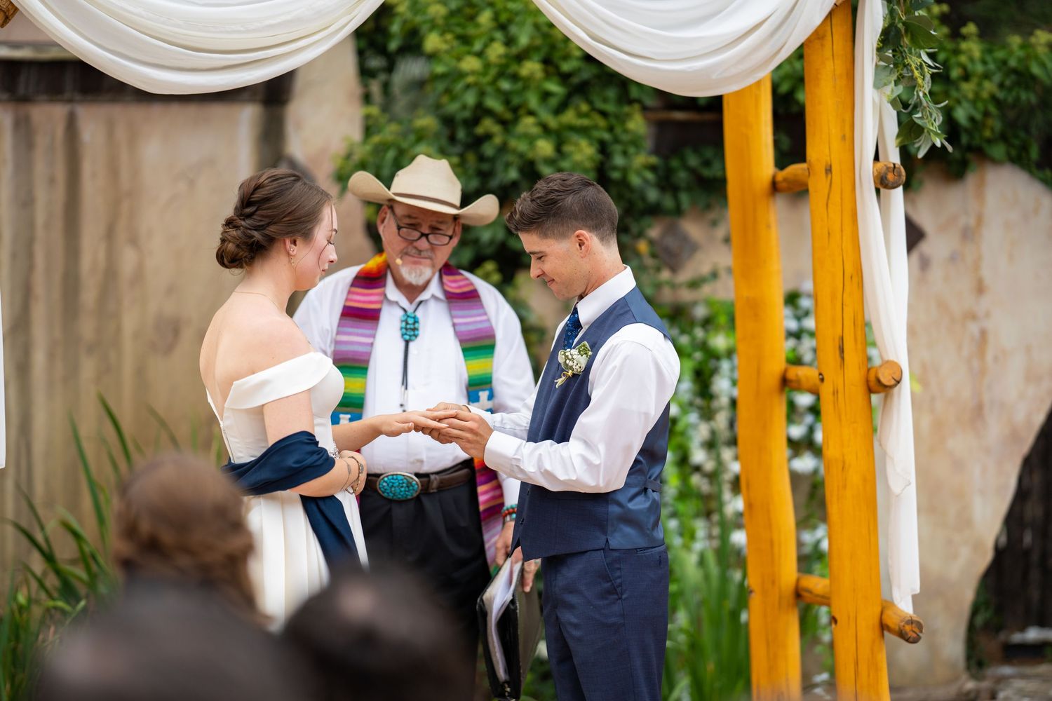 Wedding guests in formal attire gather outdoors under a yellow and white canopy during a summer celebration.