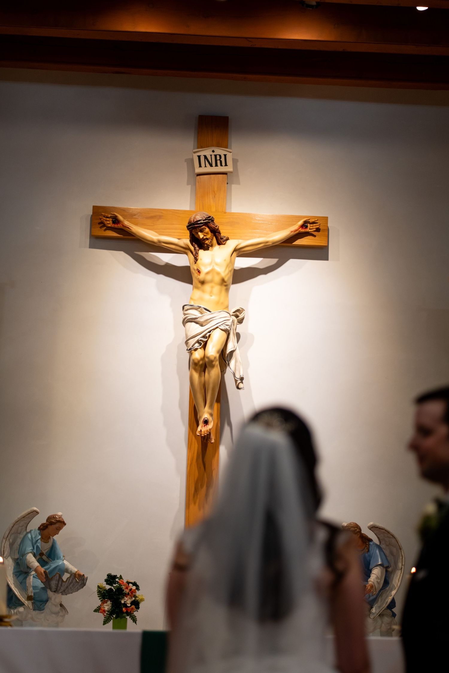 A wooden crucifix with INRI inscription displayed above a church altar during a wedding ceremony.
