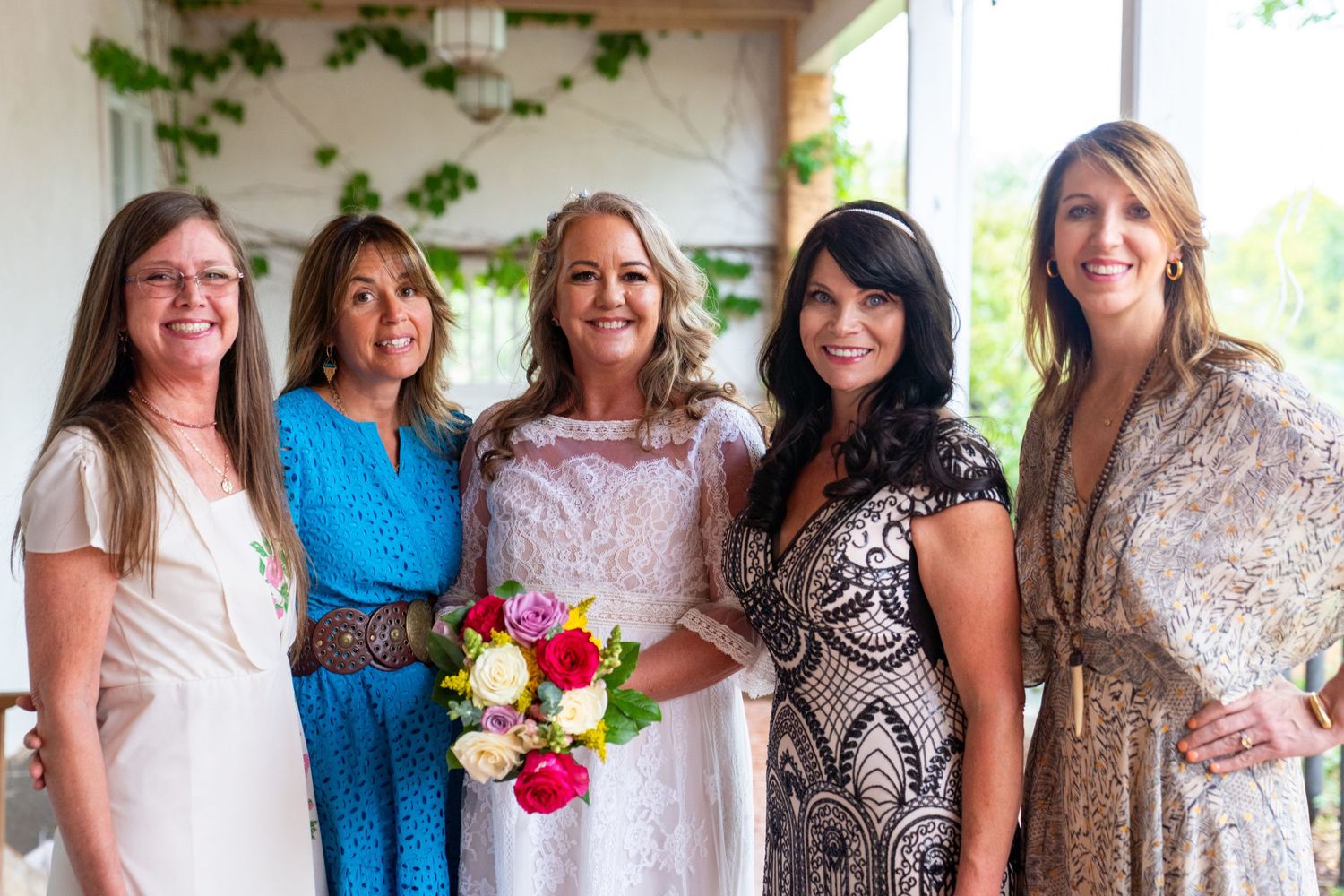 Group photo of wedding guests in coordinated dresses at an outdoor venue.