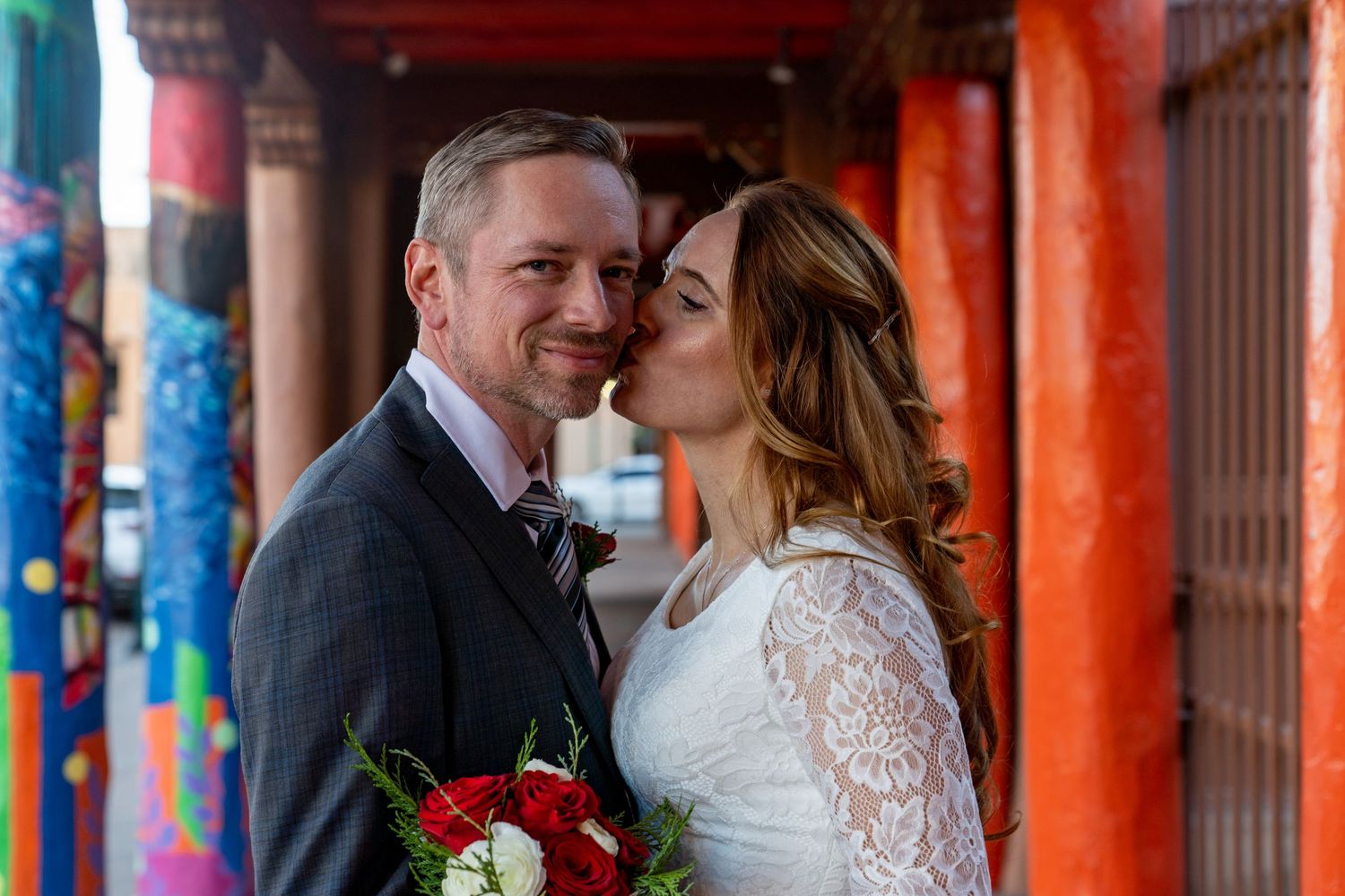 A bride and groom share a romantic moment in front of colorful columns during their wedding celebration.