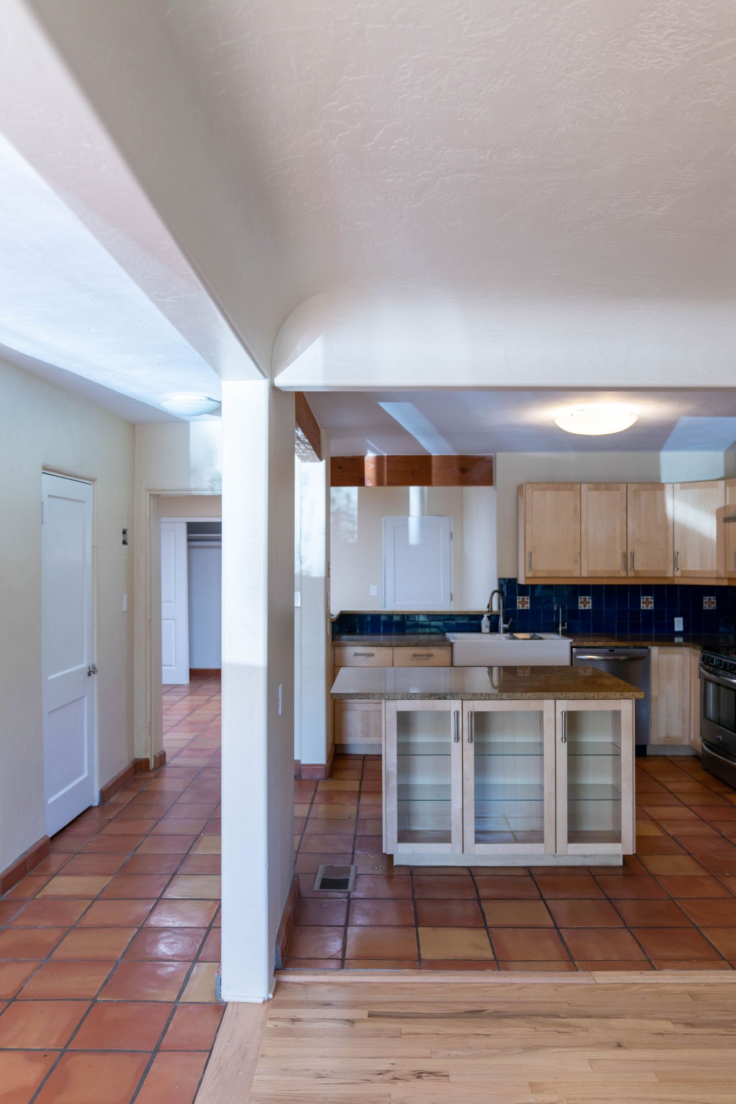 Interior view of an open basement space with terracotta tile flooring and light wood cabinets along the back wall.