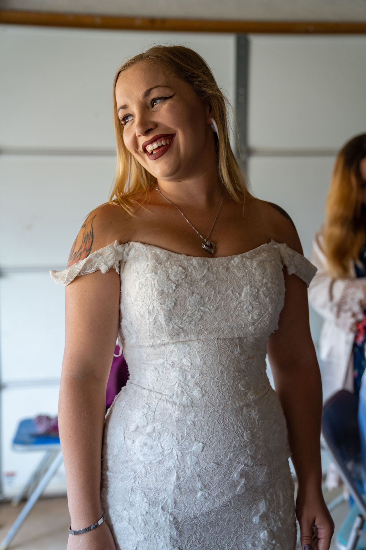 Bride wearing an elegant white lace wedding dress smiles joyfully during pre-ceremony preparations.