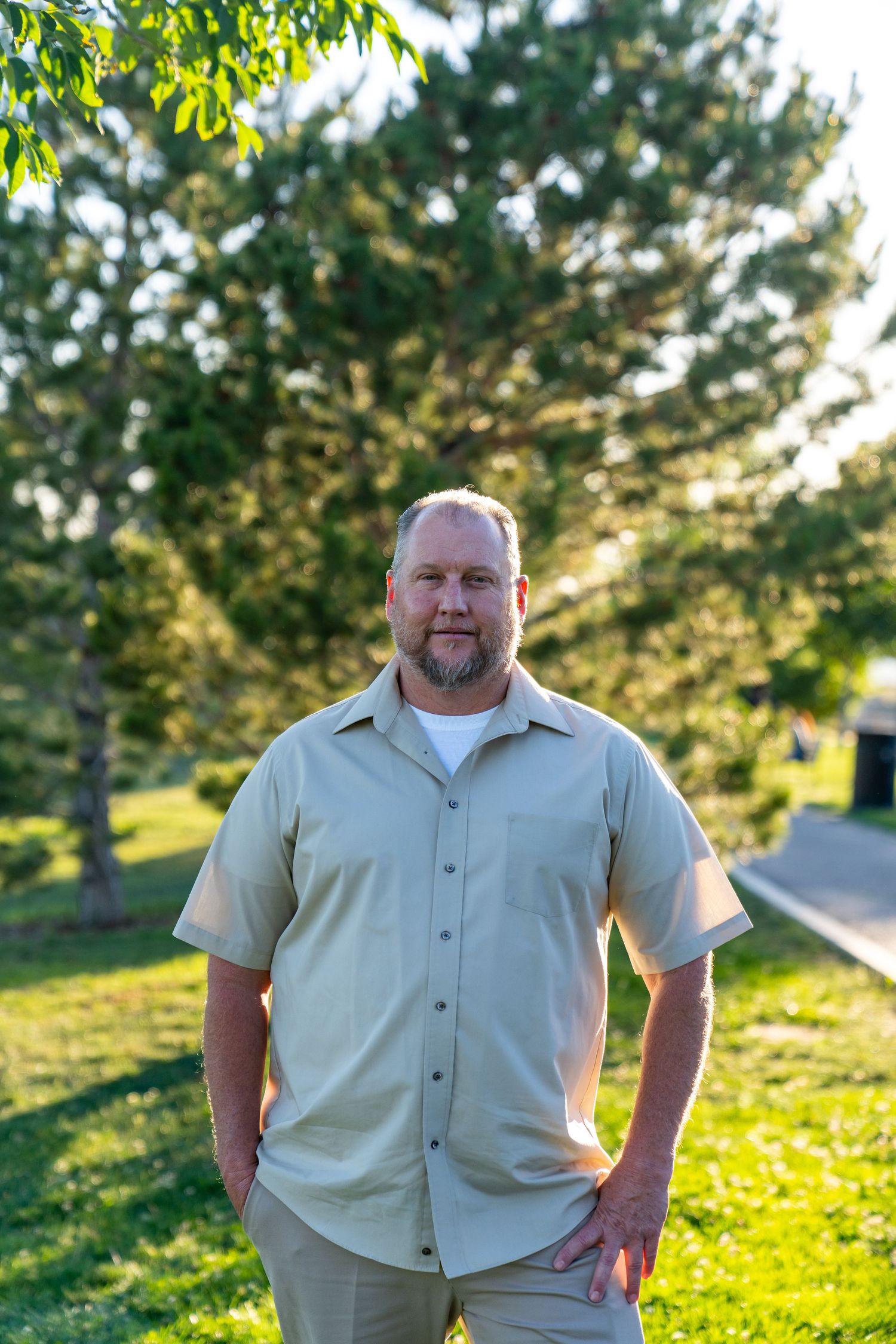 Person in light colored shirt stands in sunny park setting.