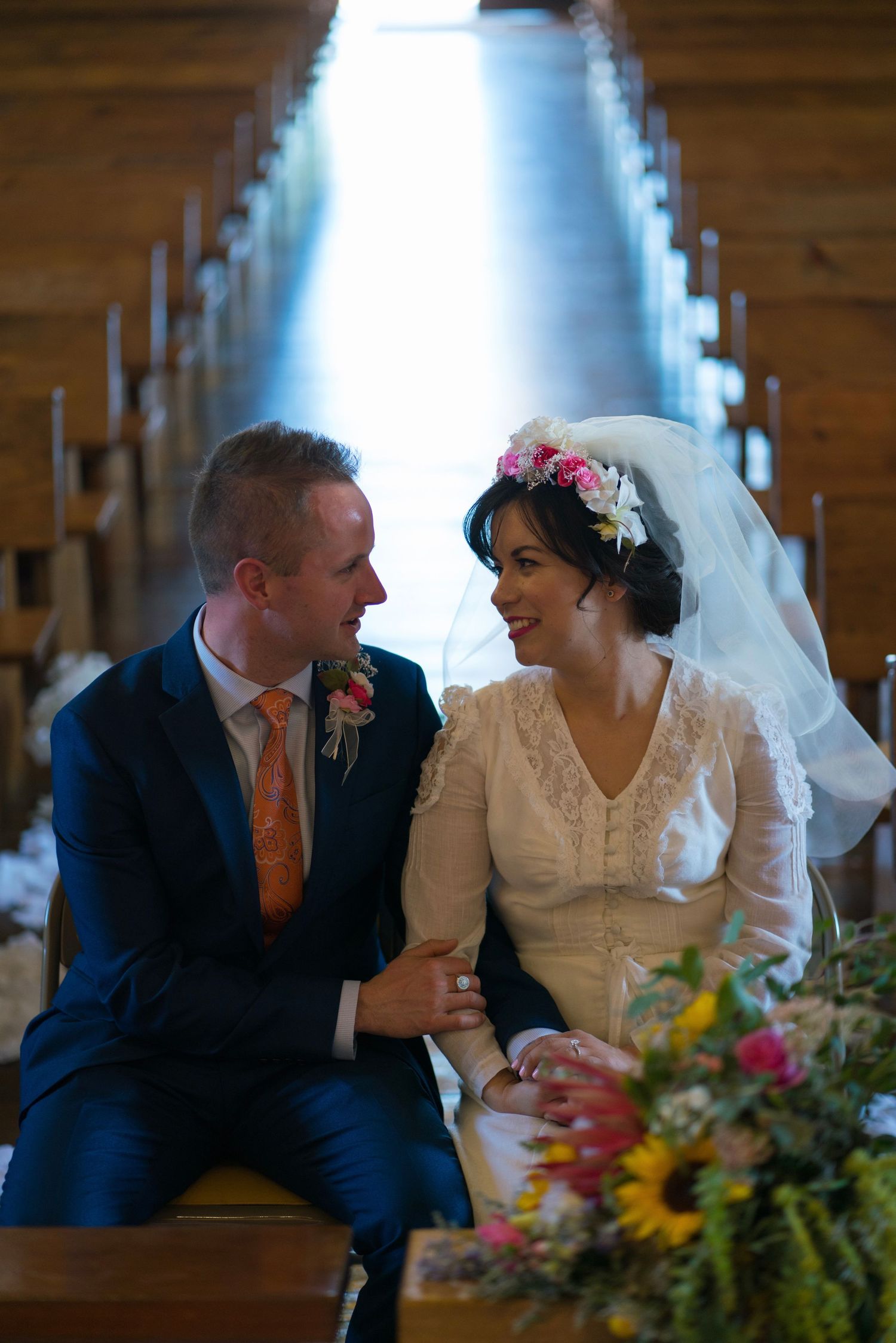 Bride and groom share intimate moments at their rustic wedding reception table decorated with colorful floral arrangements.
