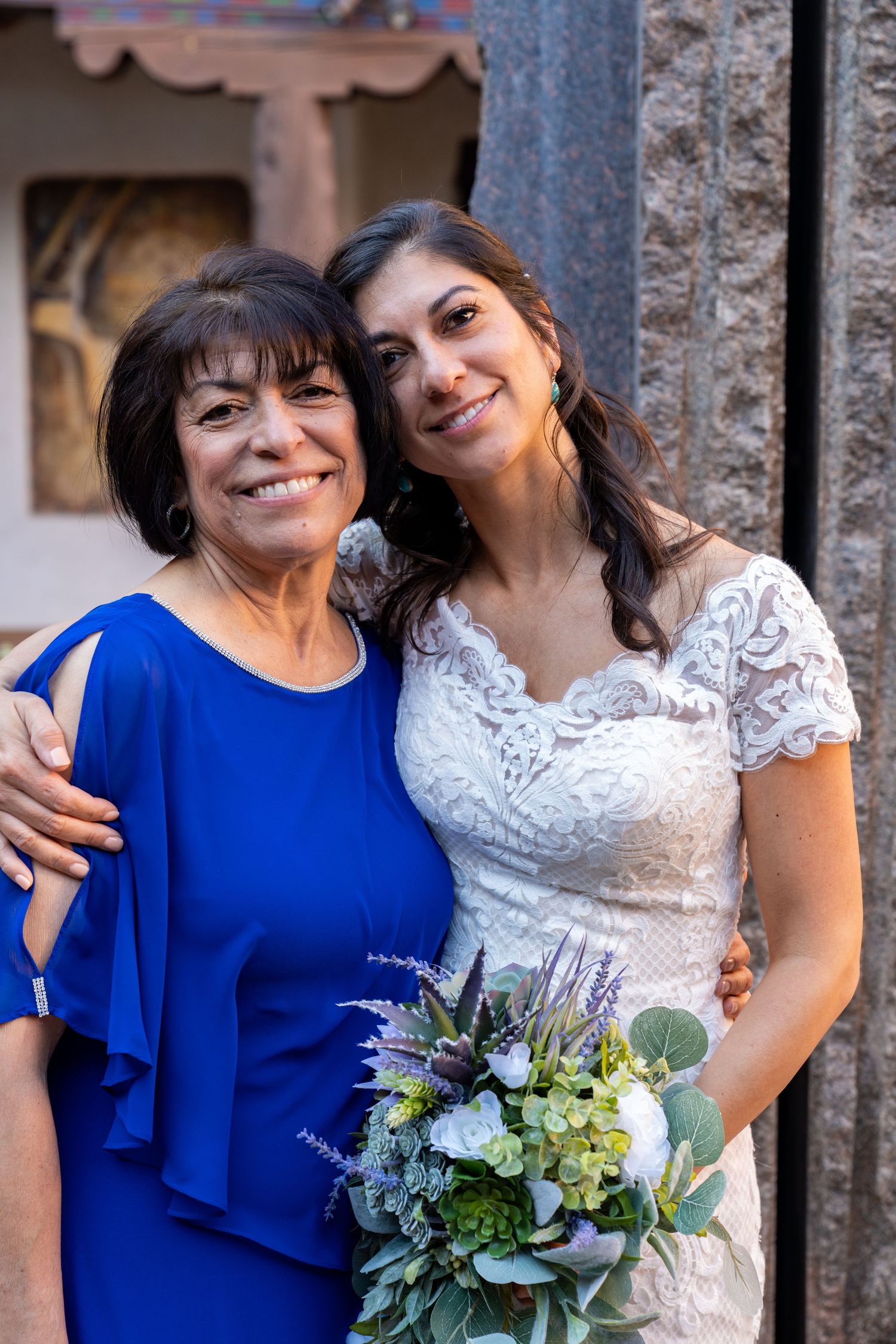 Wedding couple and guest in blue dress pose together with floral bouquet in outdoor setting.