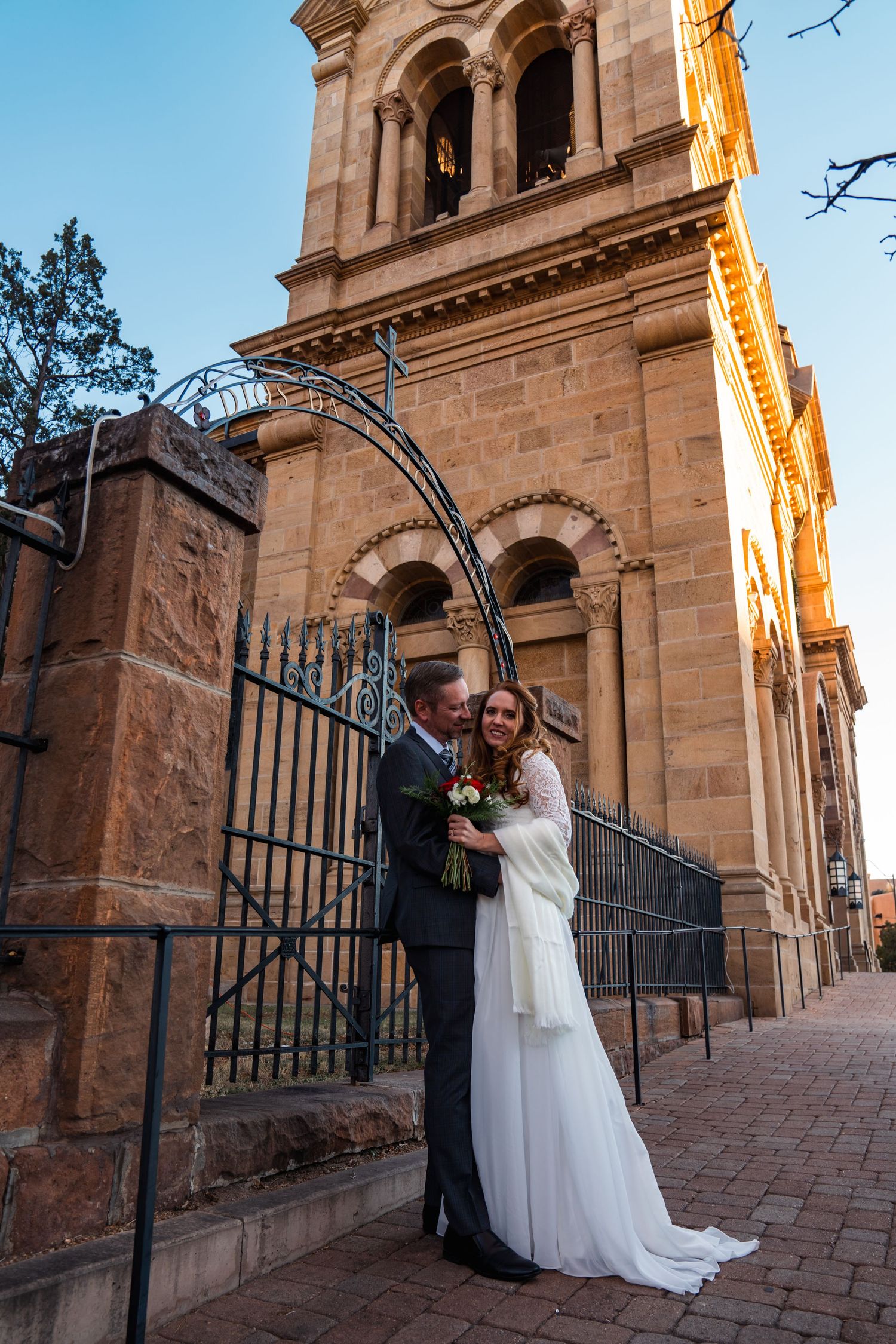 Newlyweds share romantic moments outside a historic church with ornate architecture and iron gates.