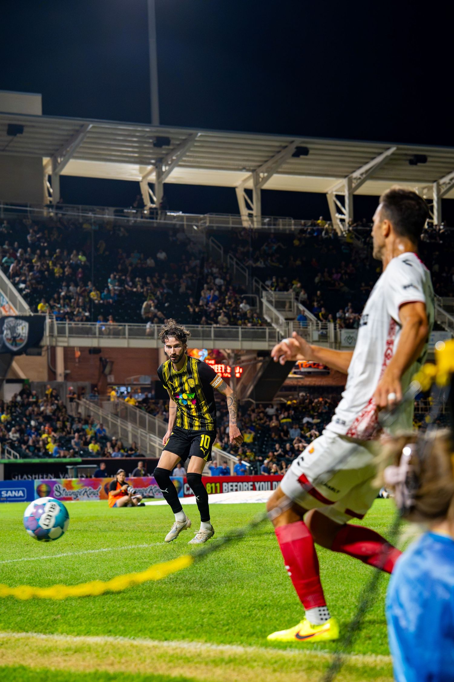 Soccer player wearing number 10 yellow jersey dribbles ball during a night match at a packed stadium.