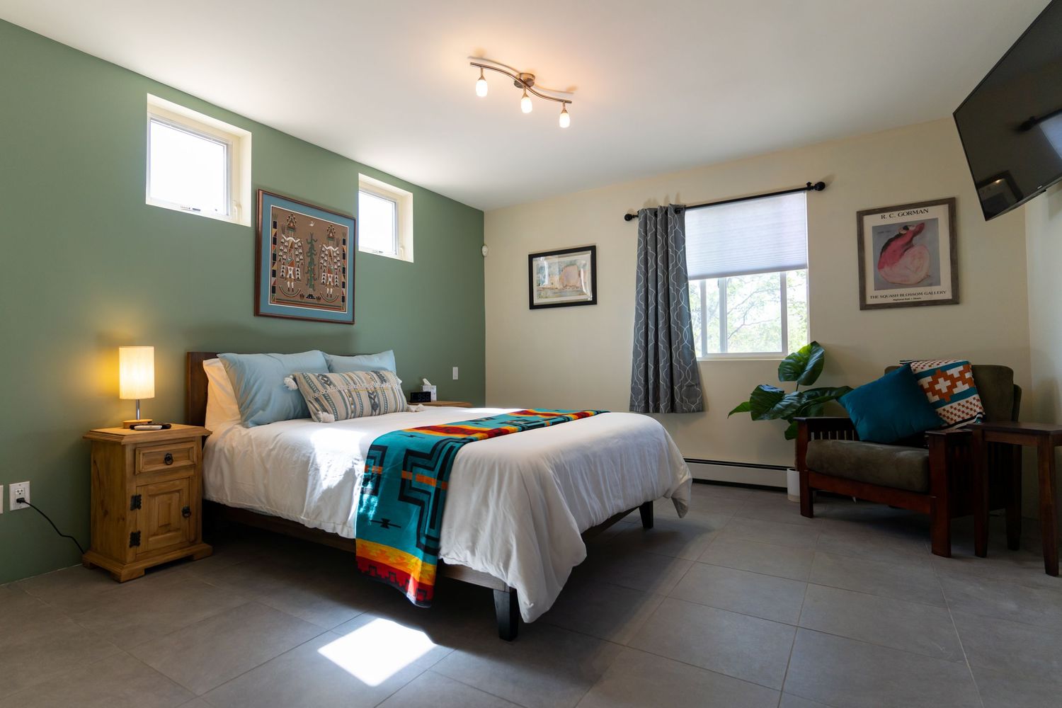 Bright and airy bedroom with teal accent wall, hardwood floors, and modern ceiling light fixture.
