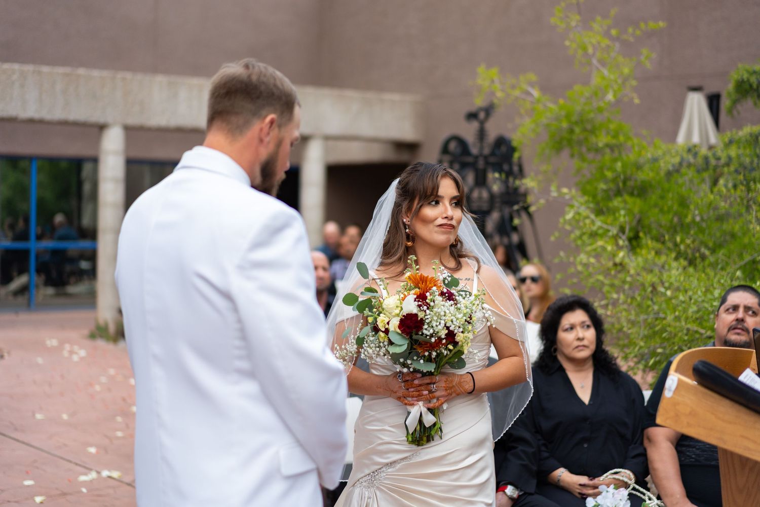 Wedding party and guests gathered outside modern building during celebration.