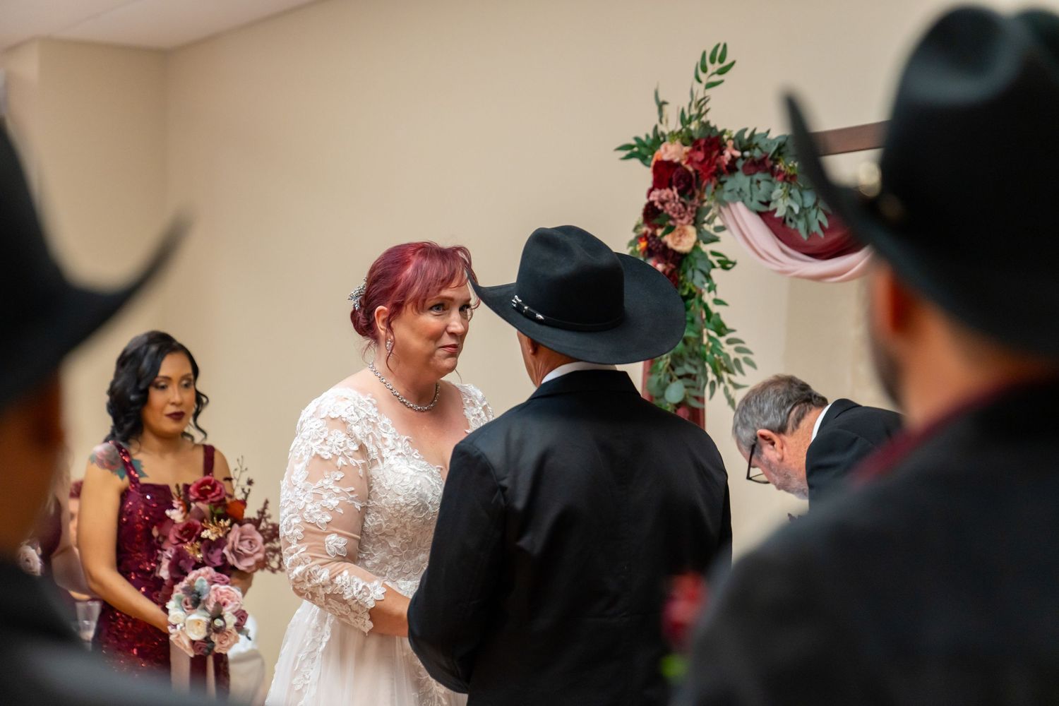 Wedding ceremony taking place under a floral arch with burgundy accents.