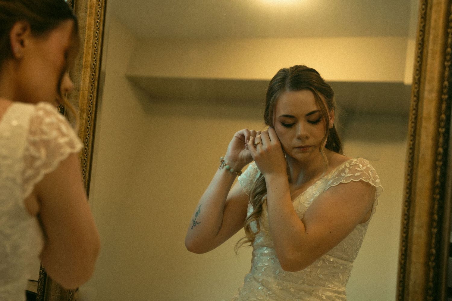 Bride getting ready in a warmly lit room with an elegant lace dress.