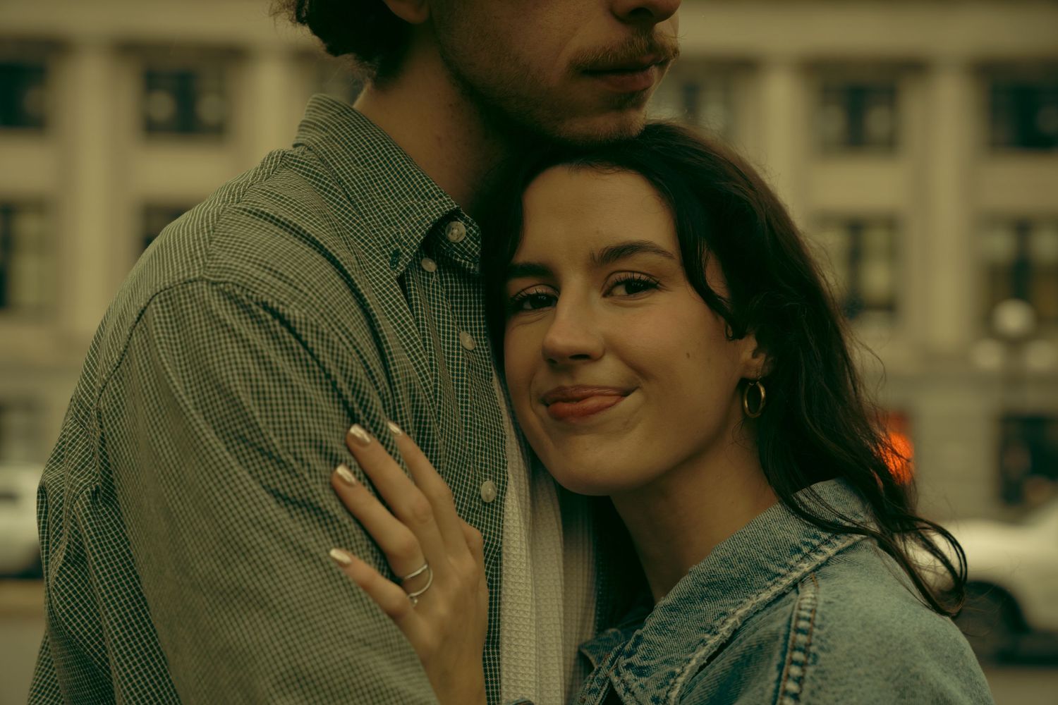 Two people in casual attire share an affectionate moment near a building.