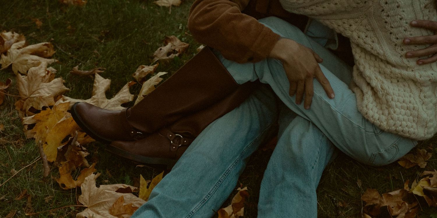 Two people sitting on grass covered with fallen autumn leaves.