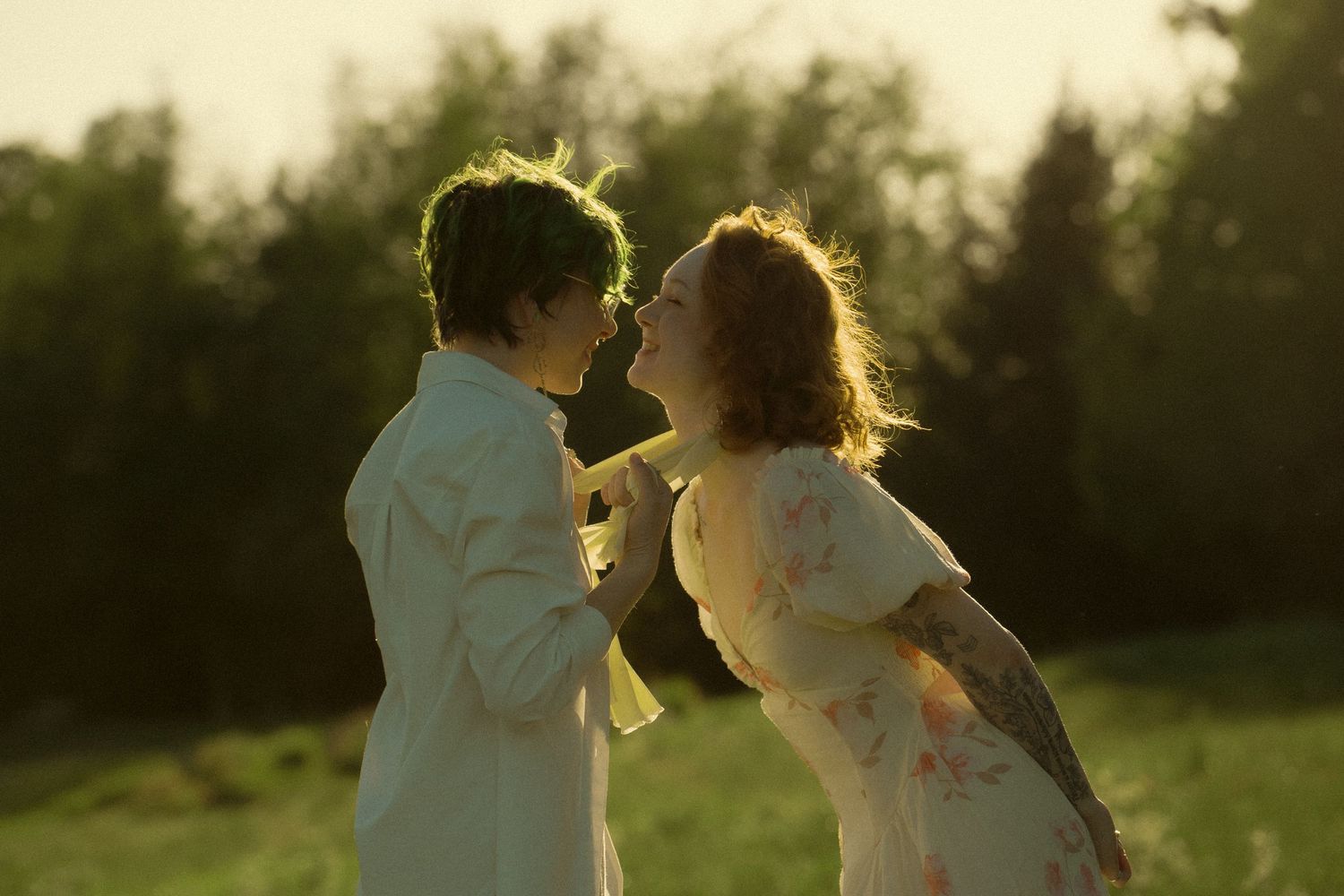 Couple sharing a romantic moment outdoors at golden hour, dressed in elegant white suit and floral dress.
