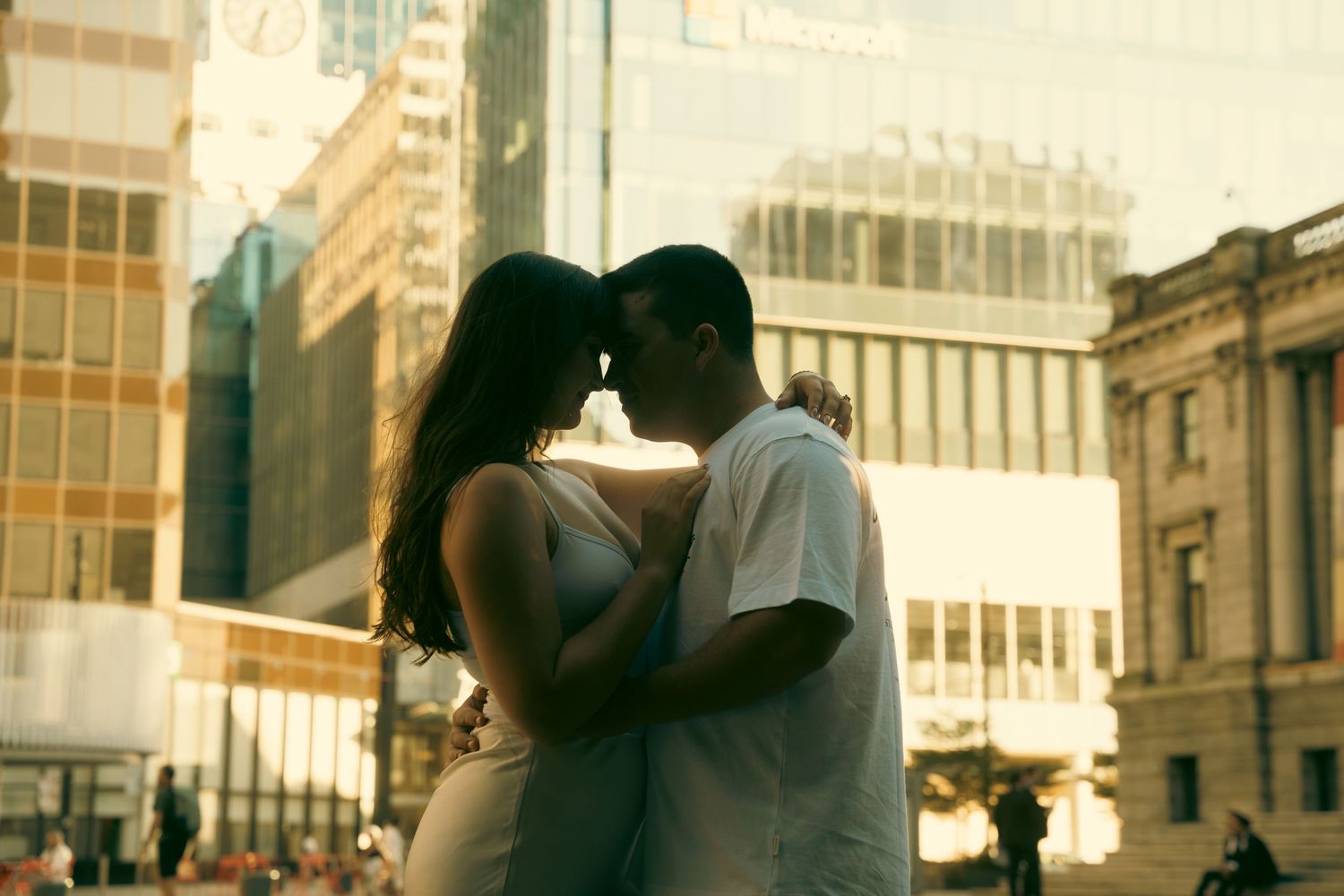 Romantic couple sharing an intimate moment in an urban cityscape with golden sunlight reflecting off modern buildings.