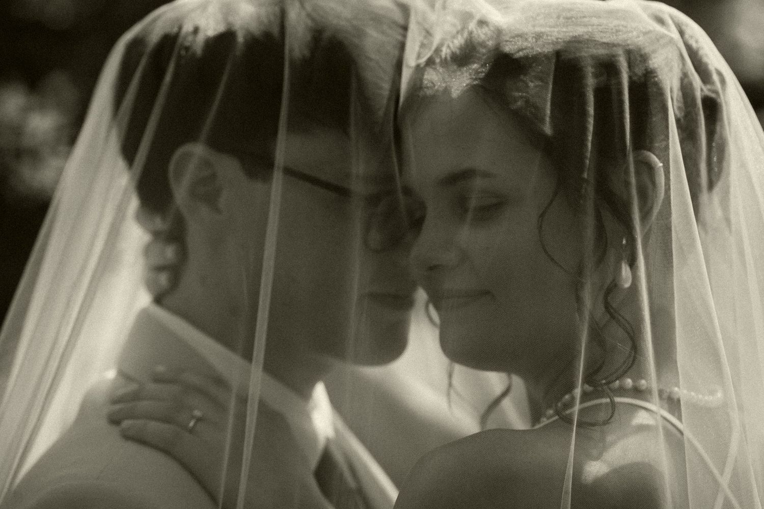 Romantic black and white portrait of bride and groom together under flowing wedding veil.