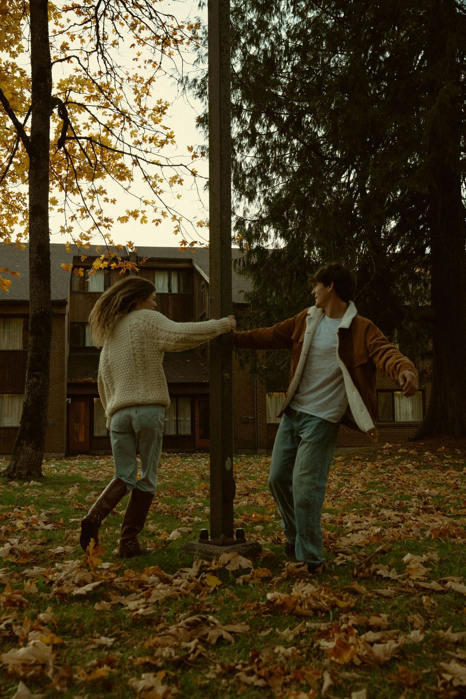 People playfully walking through a leaf-covered park during sunset.