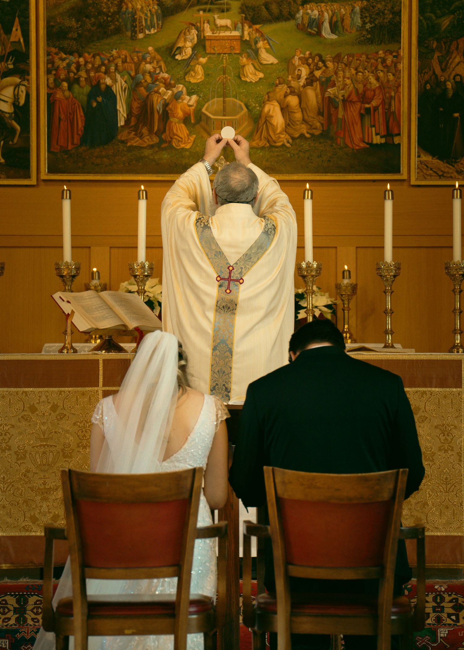A priest performs a wedding ceremony at an altar adorned with candles and religious artwork.